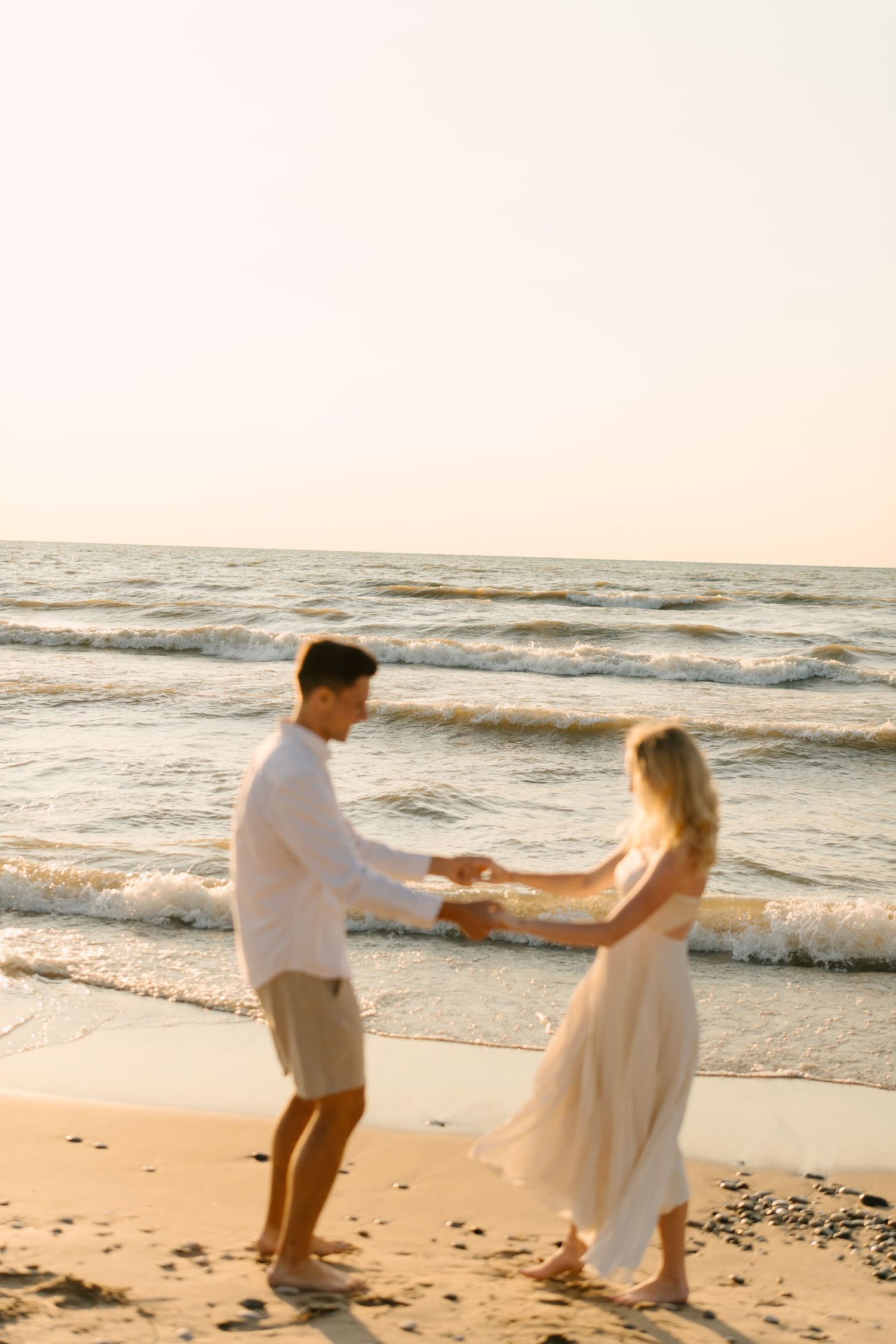 Couple dancing and holding hands at the waters edge at sunset on a sandy ocean beach.