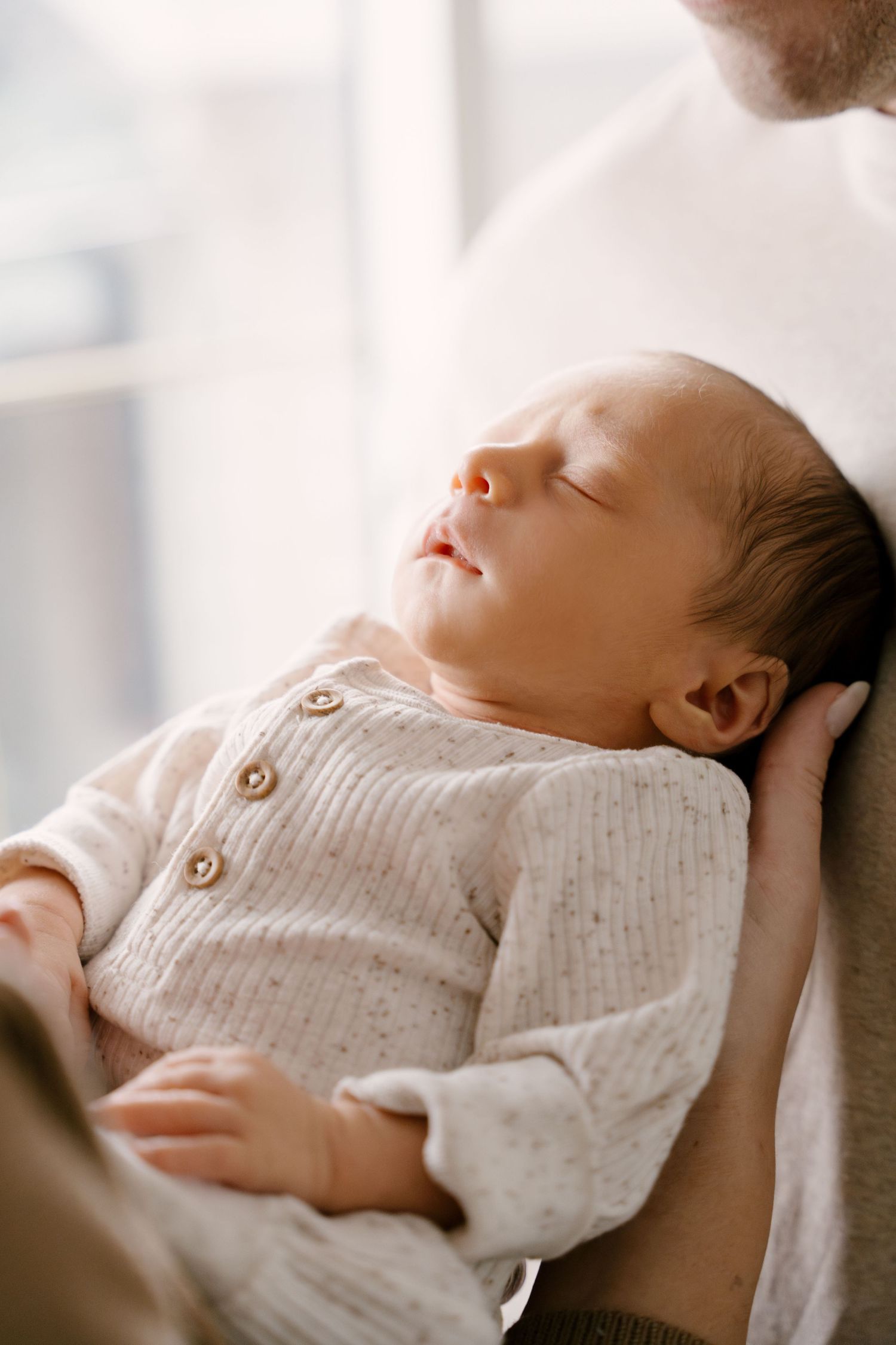 Peaceful newborn baby sleeping in fathers arms wearing a cream knit button onesie.