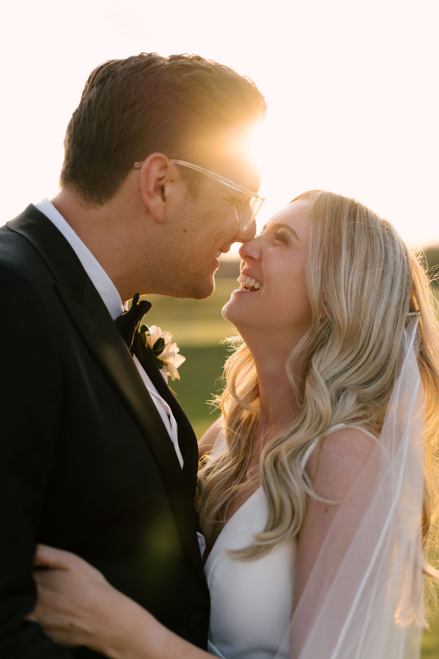 Bride and groom share a joyful moment at golden hour, faces close, she in veil, he in black tuxedo at Whistle Bear.