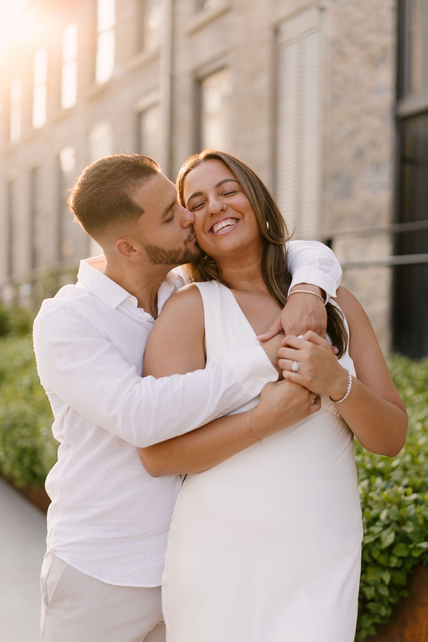 Man embracing and kissing woman on cheek as she smiles joyfully in warm golden sunlight.