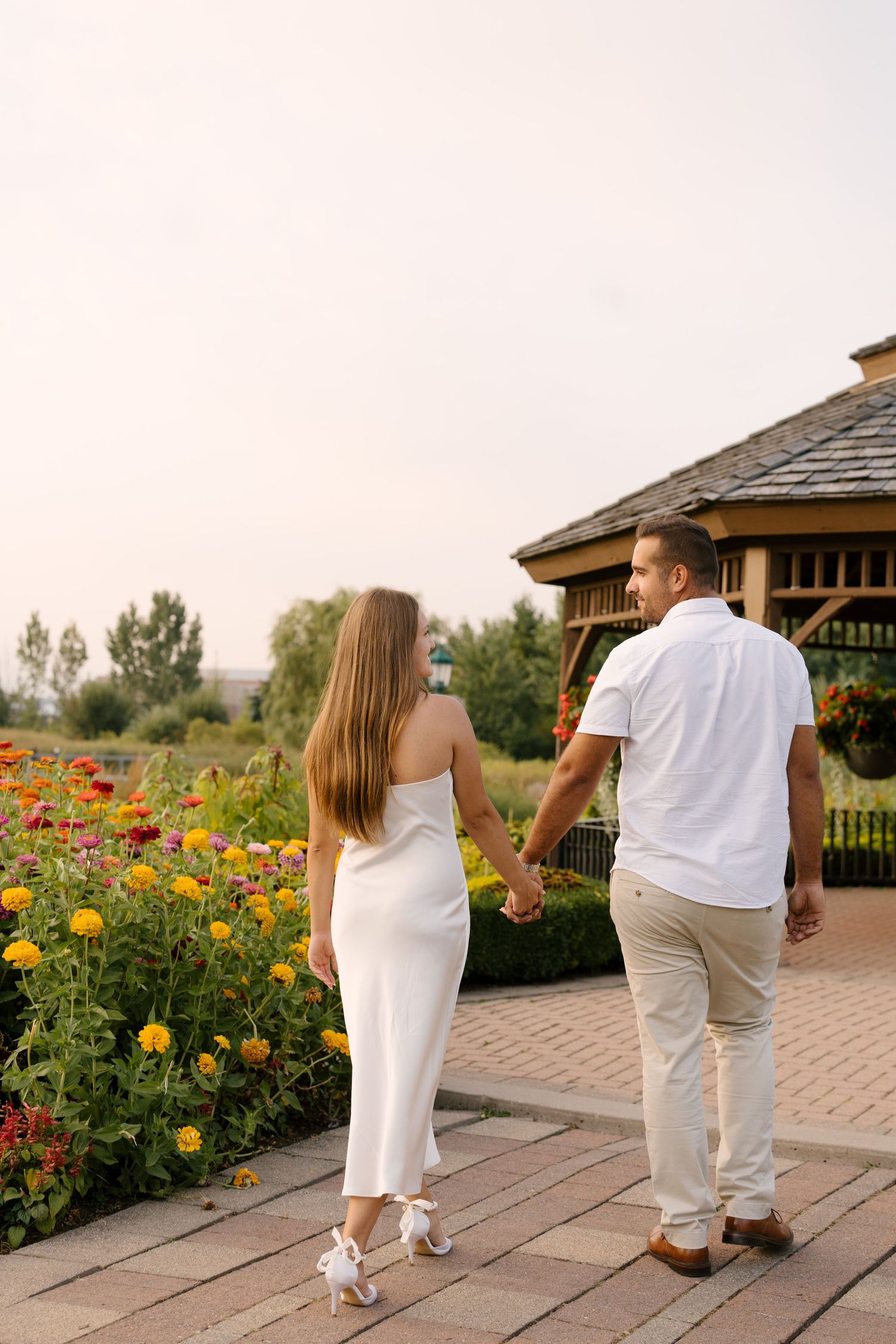 Couple holding hands walking through a colorful garden path toward a wooden gazebo.