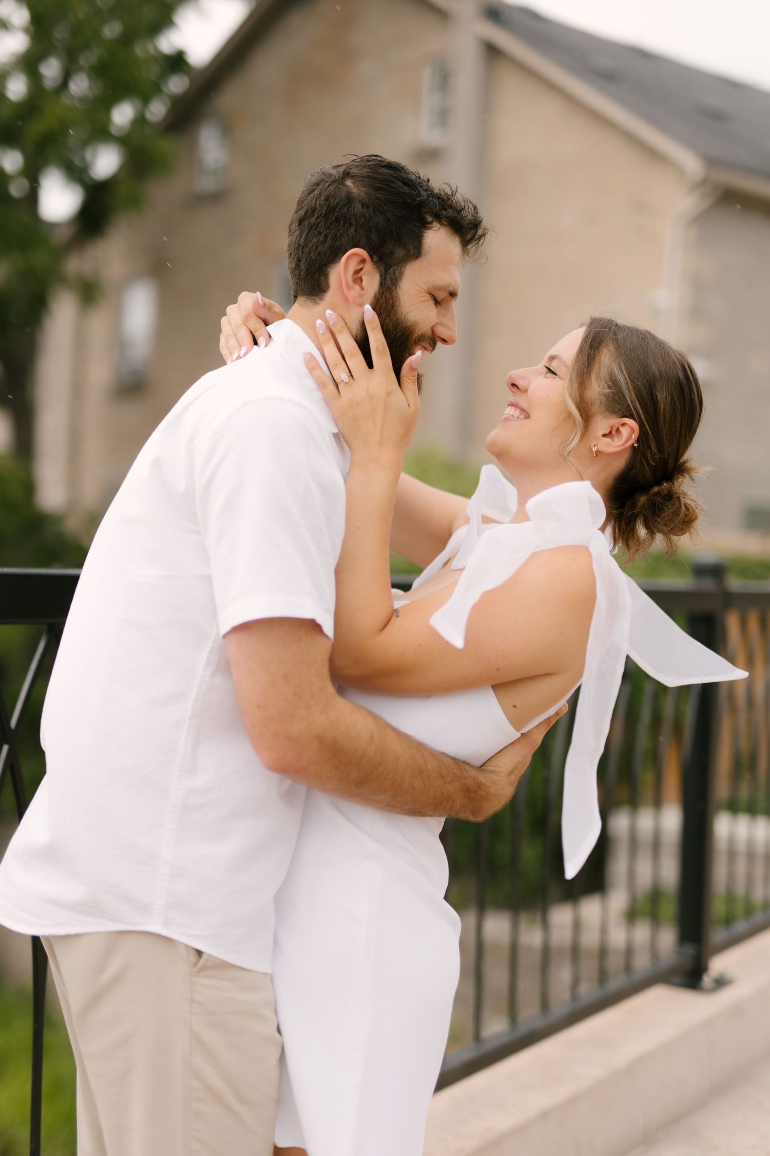 Happy couple in white outfits embracing and smiling at each other on an outdoor balcony.