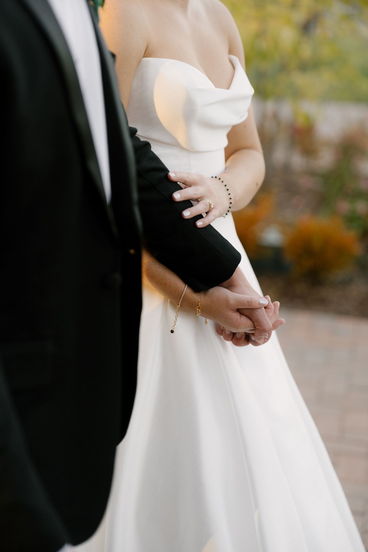 Close-up of bride and groom holding hands, bride wearing white strapless gown and bracelet at Pillar and Post.