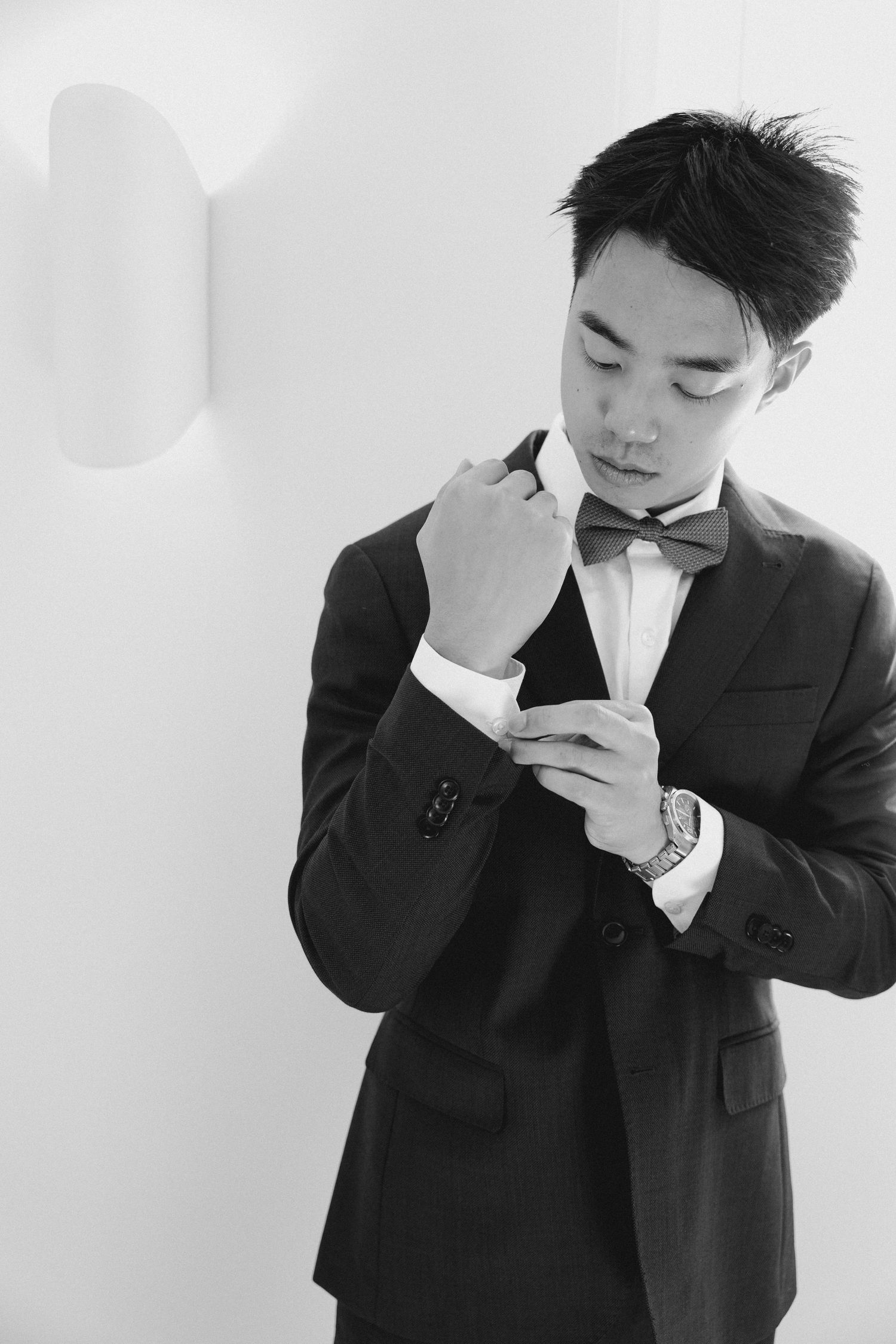 A dapper groom in a black suit adjusts his bow tie in a black and white portrait photo at Wren House.