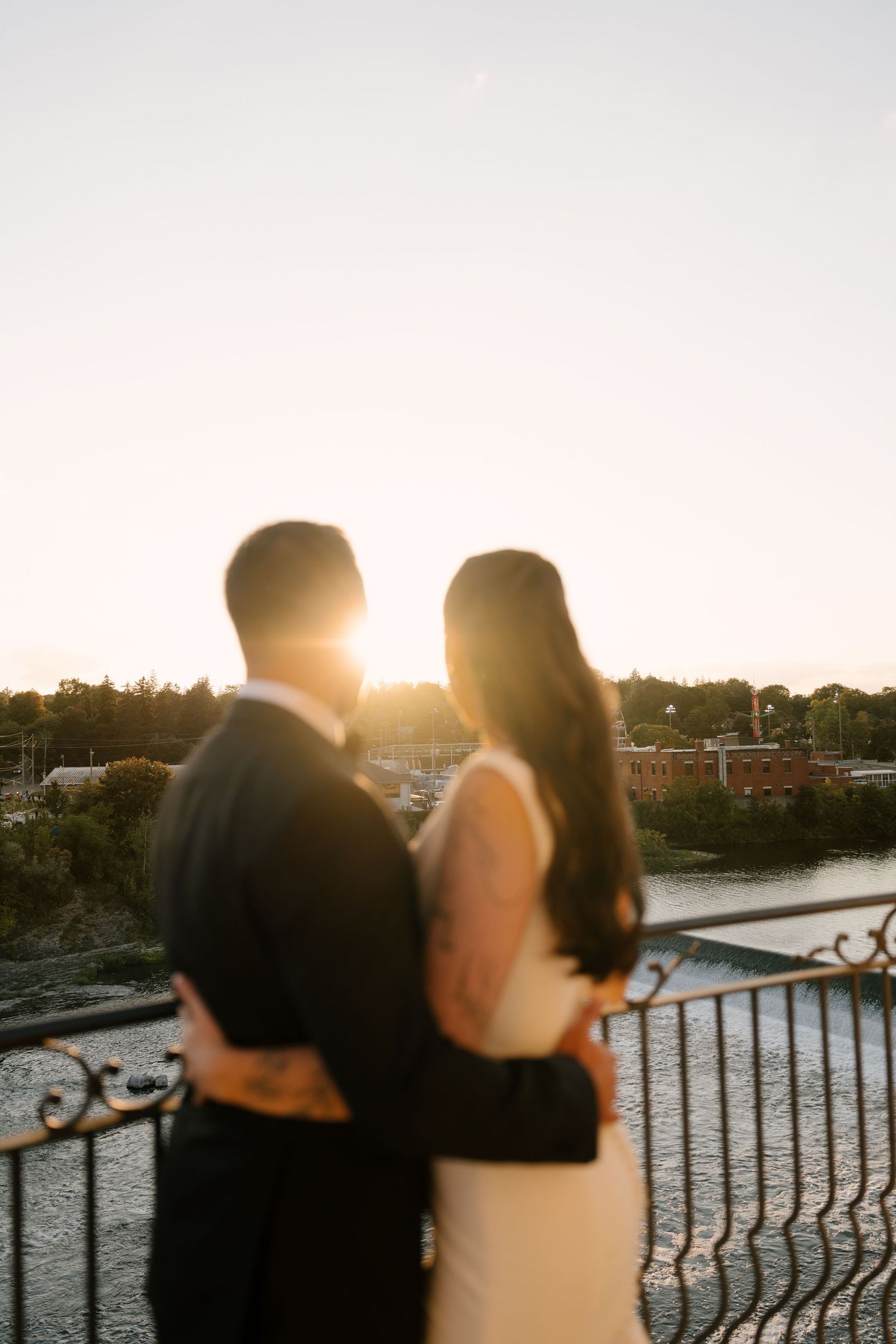 Bride and groom silhouetted against a golden sunset overlooking a scenic waterway at Cambridge Mill.