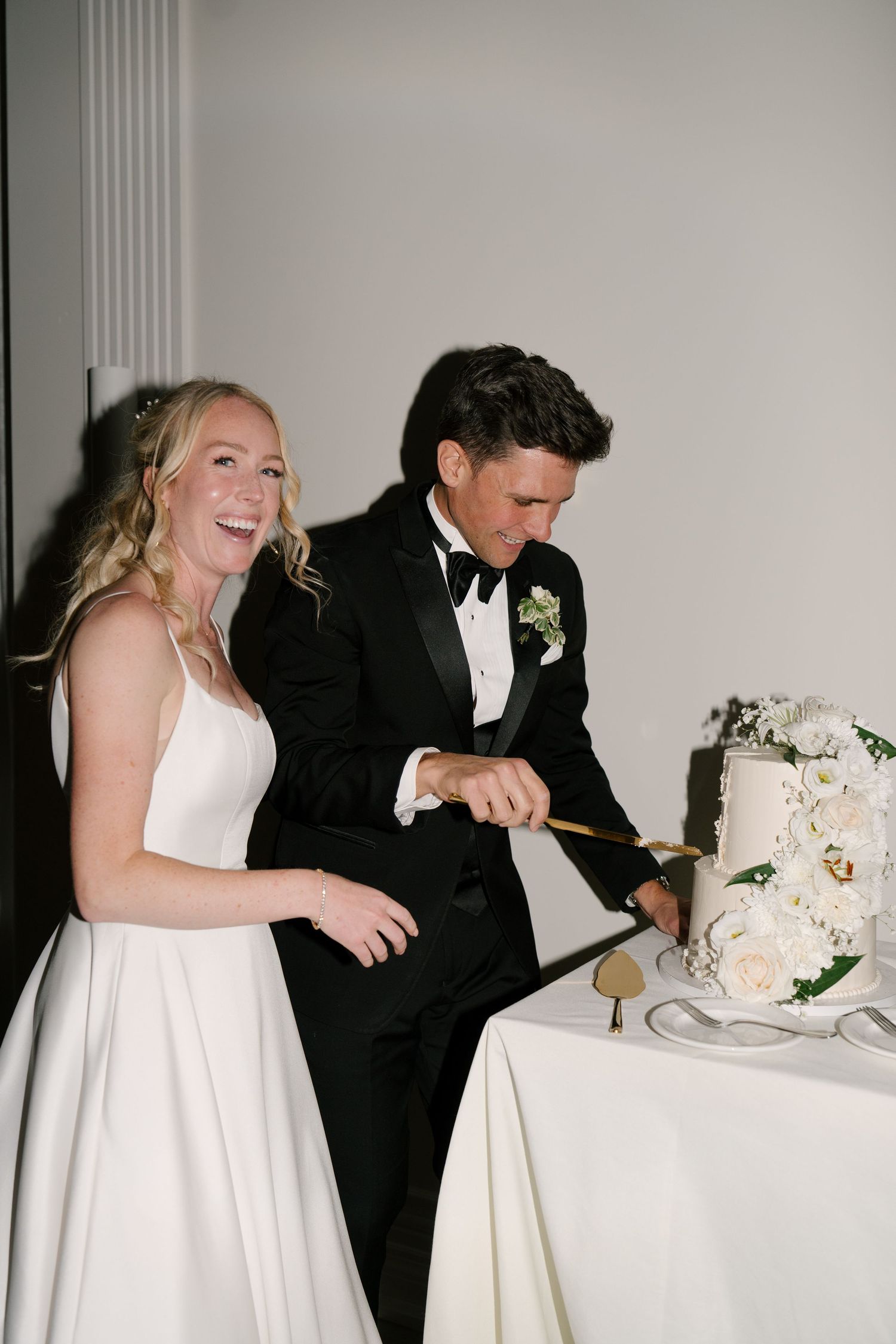 Laughing bride and groom cutting their white floral wedding cake at the reception at Roseville Estates wedding venue.
