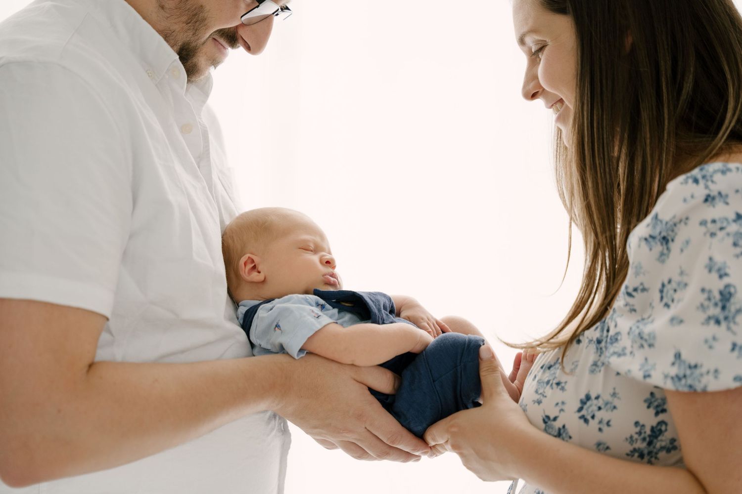 New parents holding their sleeping newborn baby together in bright room.