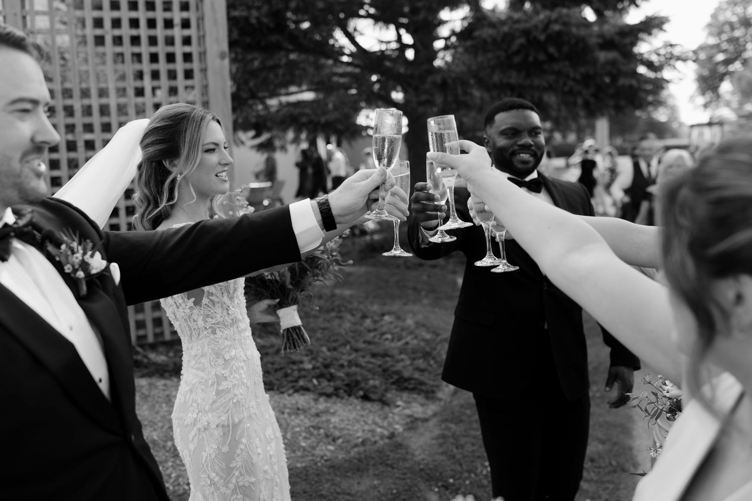 Bride and groom toasting champagne glasses with wedding guests in a joyful black and white photo.