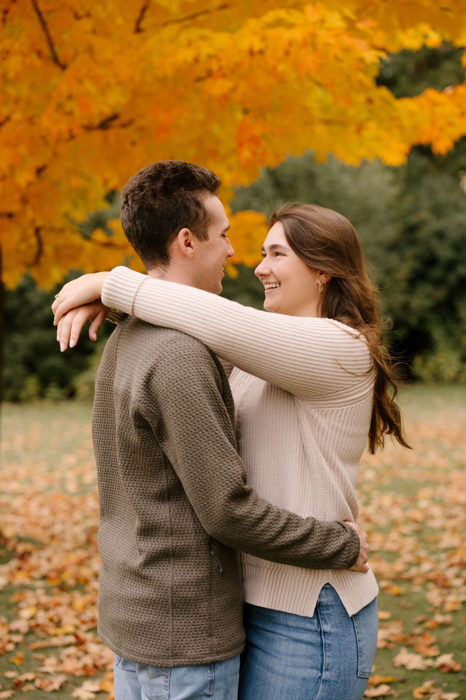 A joyful couple embraces and smiles at each other beneath a brilliant yellow autumn tree.