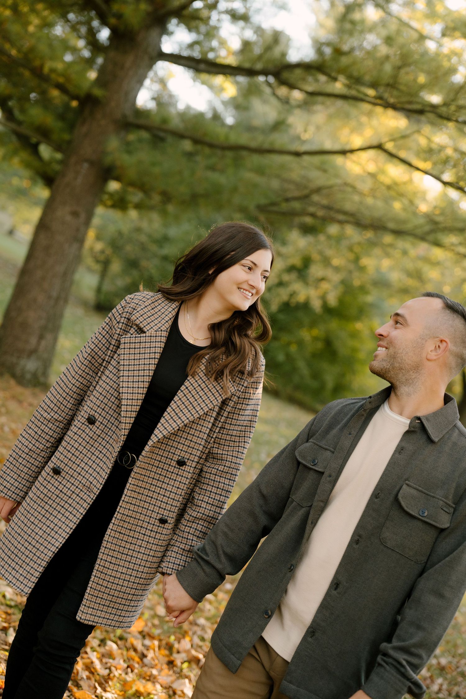 Happy couple holding hands and gazing at each other among colorful autumn trees in park.