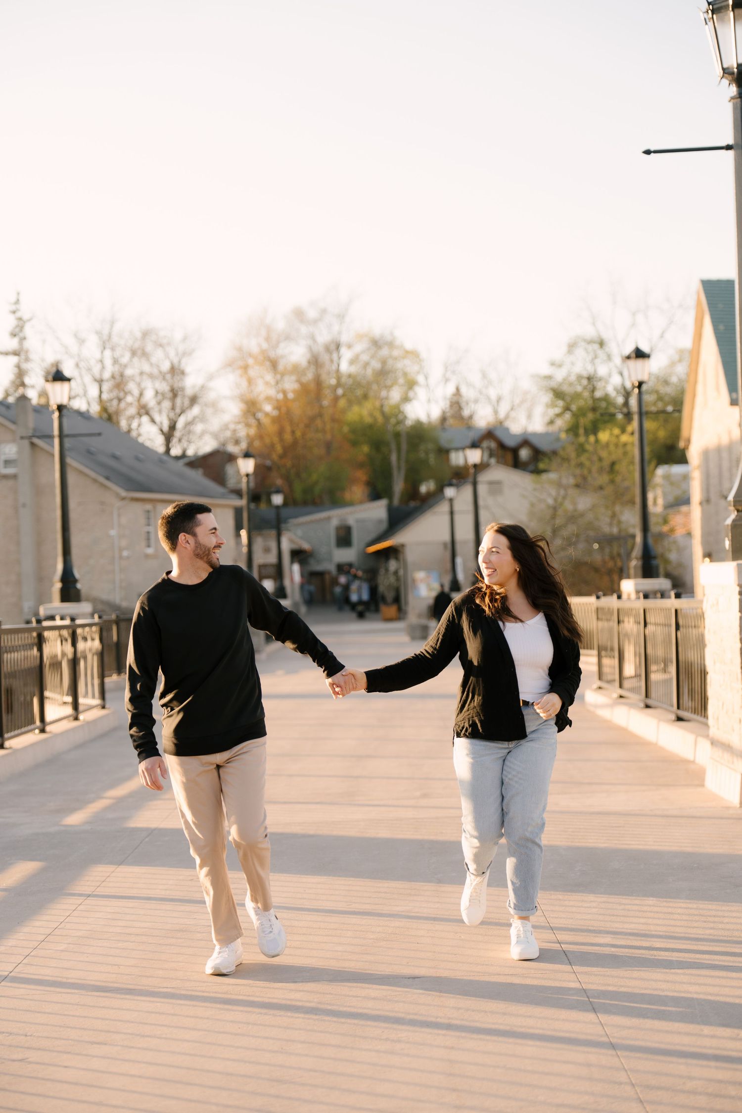 Happy couple strolling hand in hand along a sunlit pedestrian bridge with street lamps.
