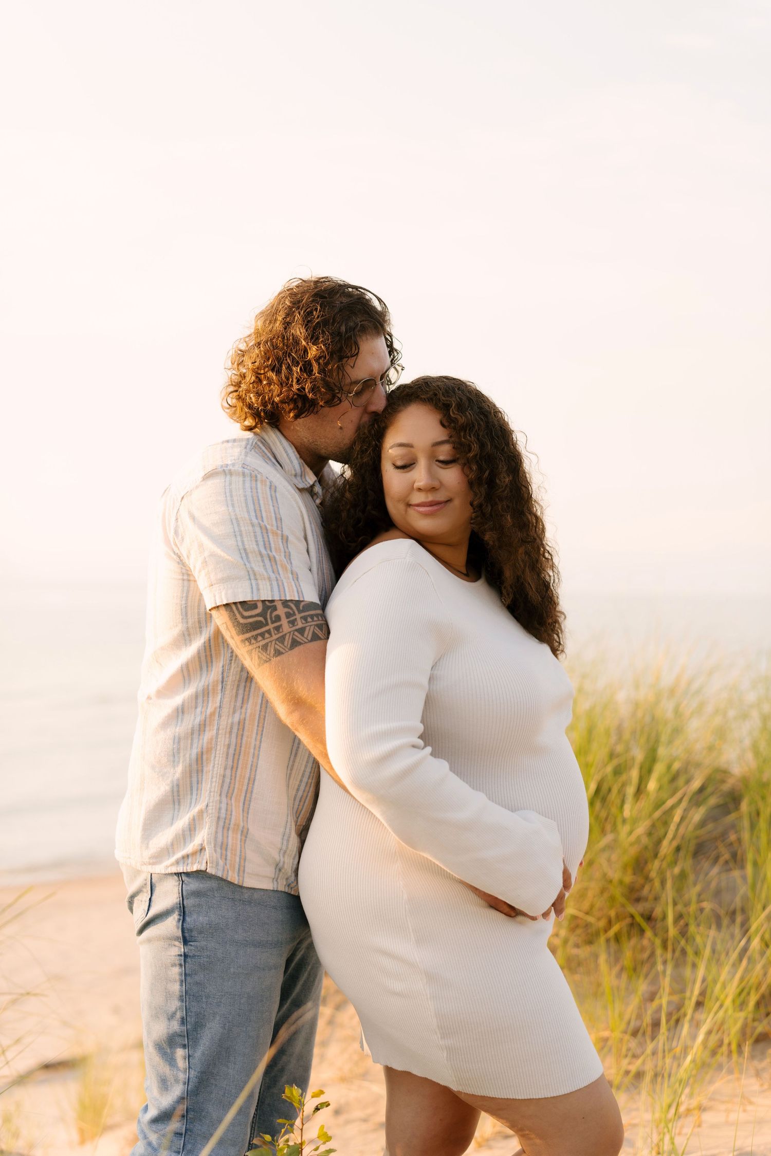 Expecting couple embracing on a sandy beach at golden hour during maternity session.