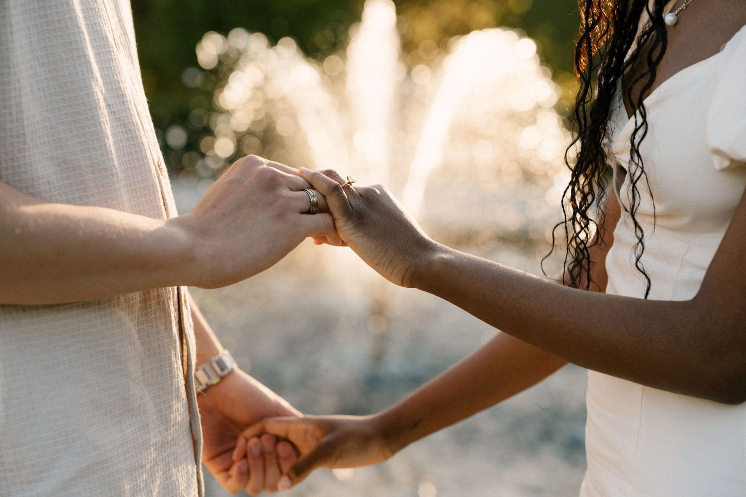 Close-up of couple exchanging a ring near a glowing fountain in warm sunset light.