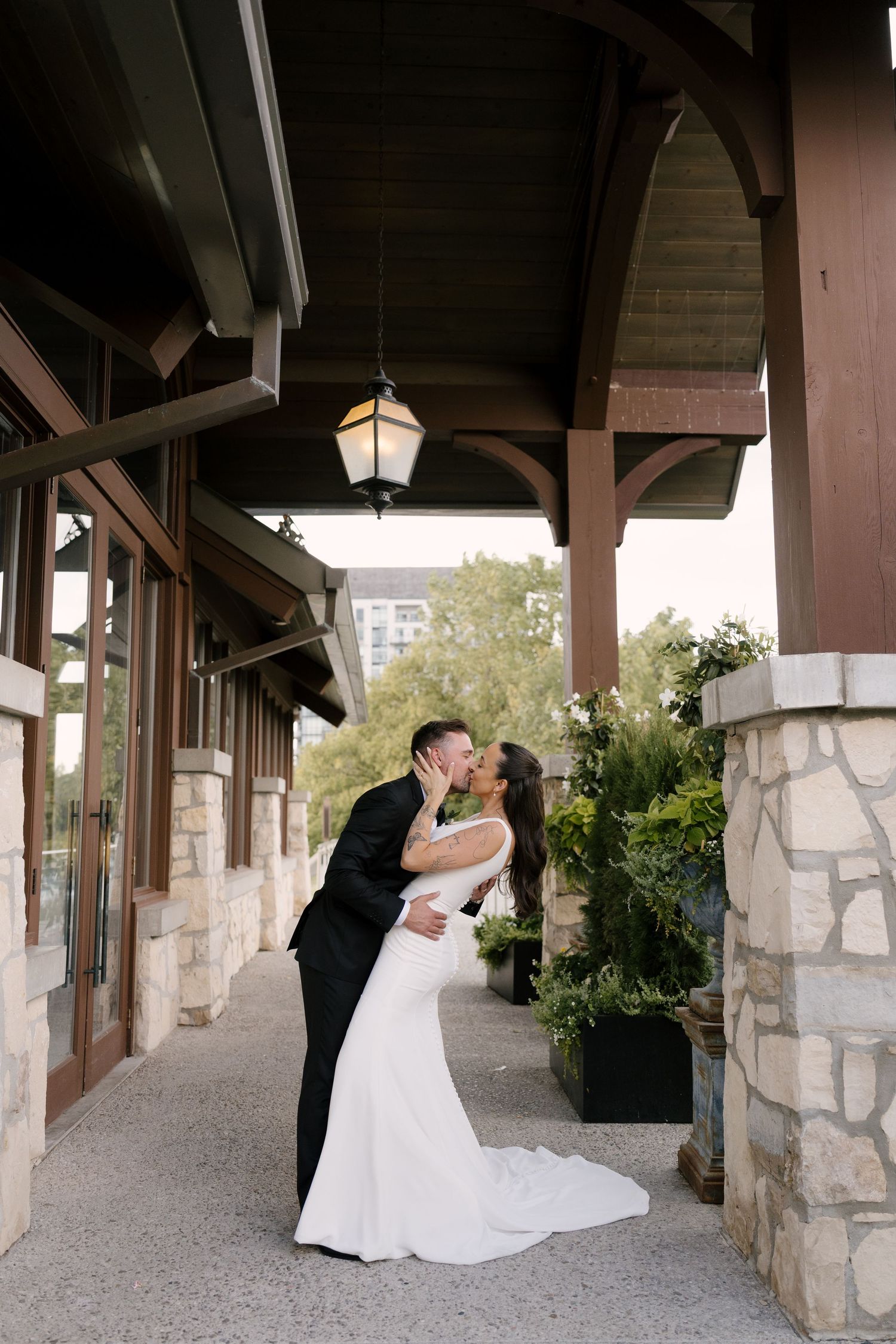 Bride and groom share a romantic dip kiss under a wooden pergola with hanging lanterns at Cambridge Mill.