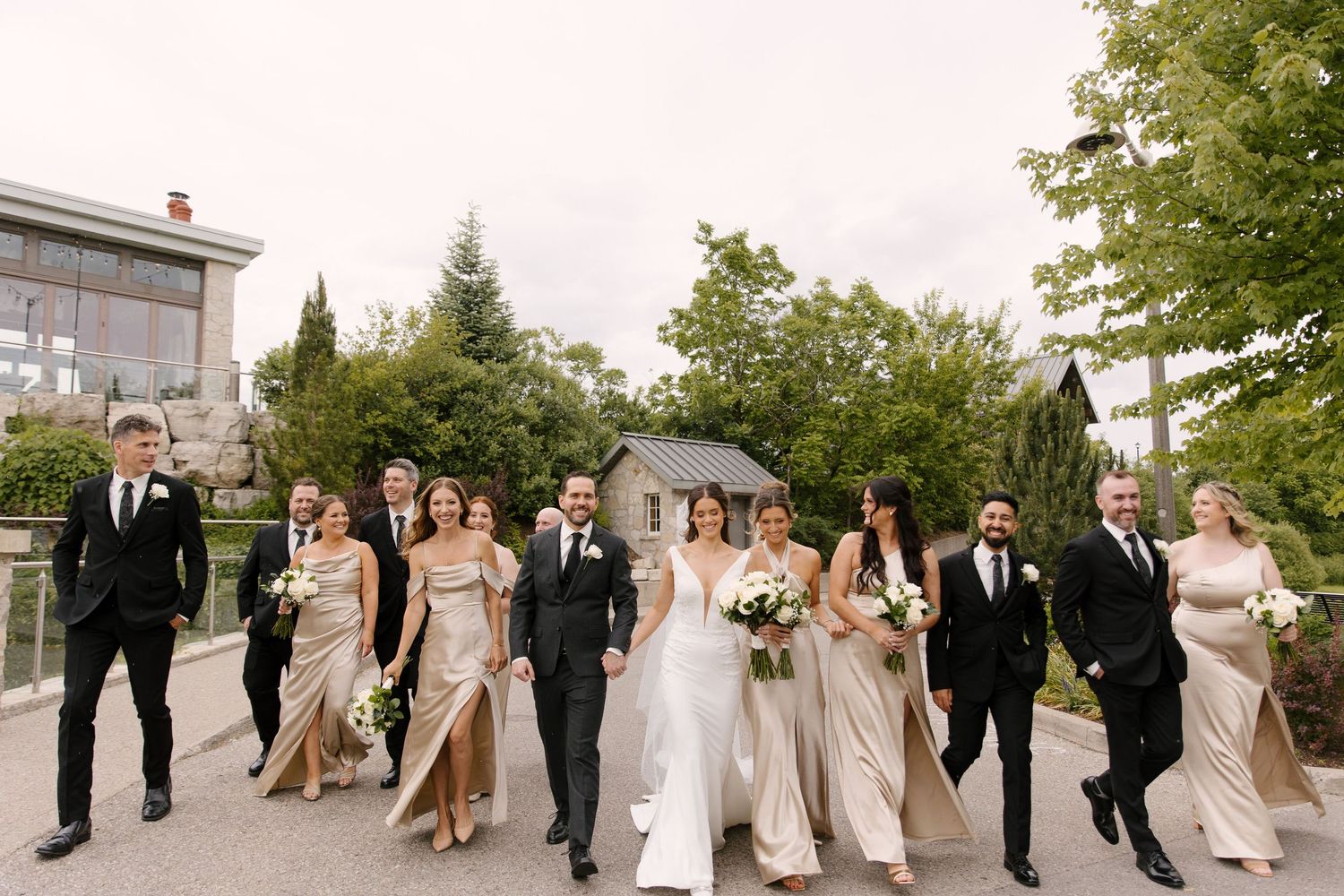 Wedding party walking confidently together outdoors in elegant black and champagne attire at Cambridge Mill venue.