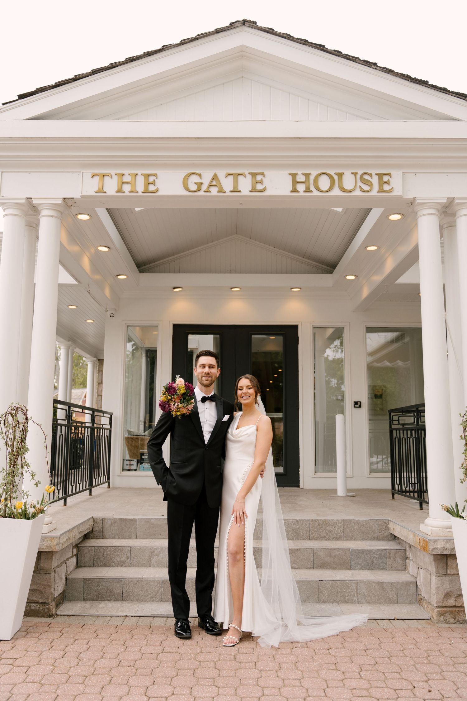 Bride and groom pose on steps outside The Gate House venue, dressed in wedding attire.