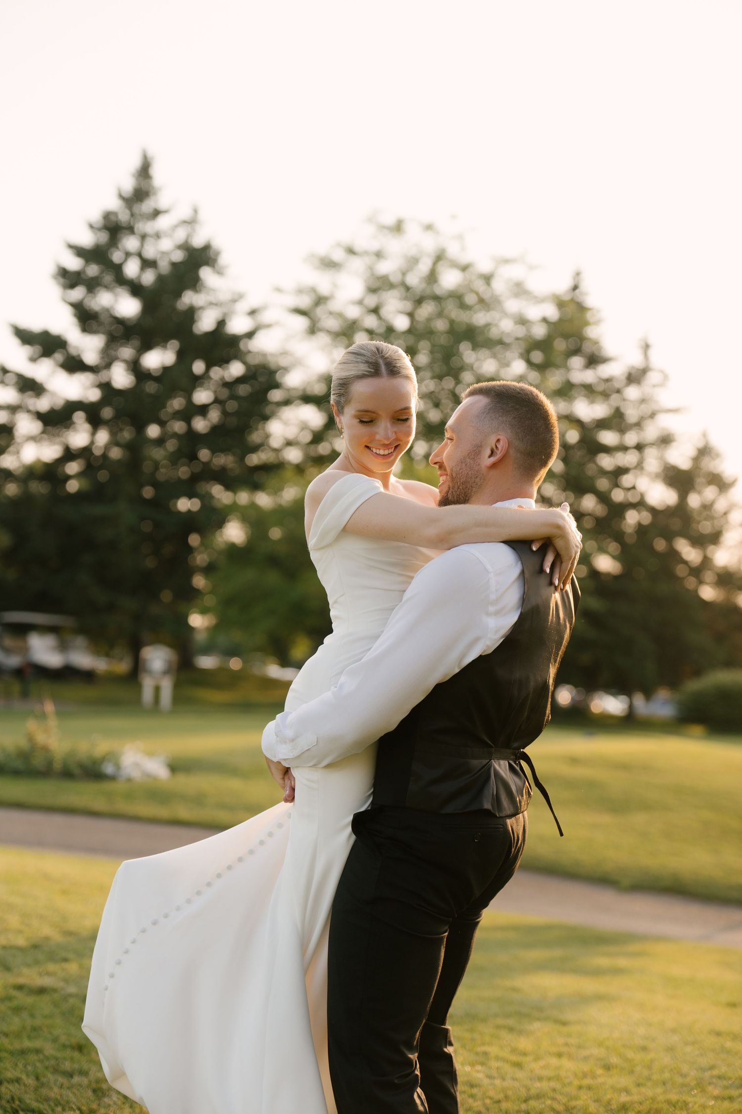 Groom lifting bride in white wedding gown during golden hour outdoor portrait on lush green lawn in Guelph.