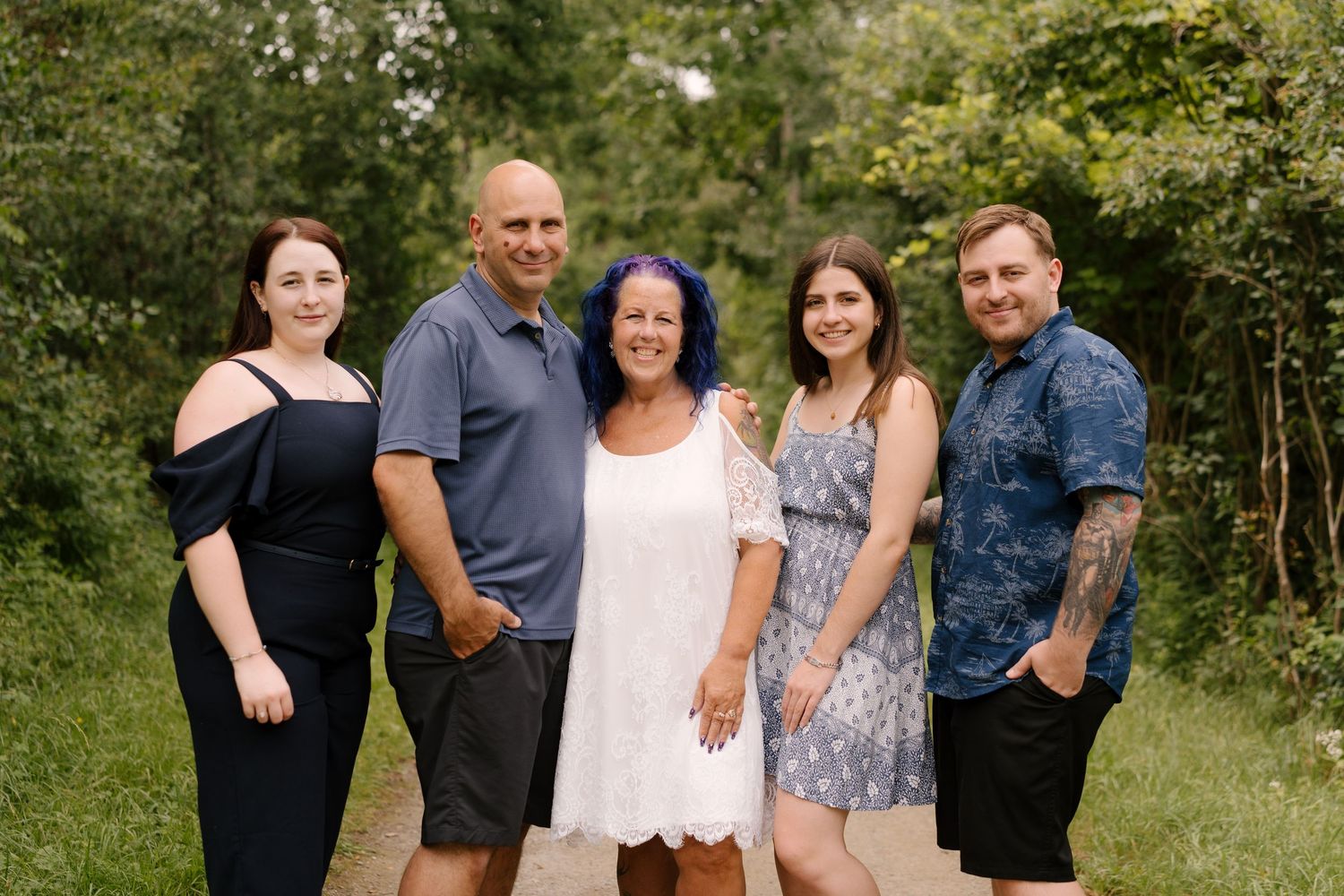 Family of five smiling together on a wooded path during an outdoor photo session.