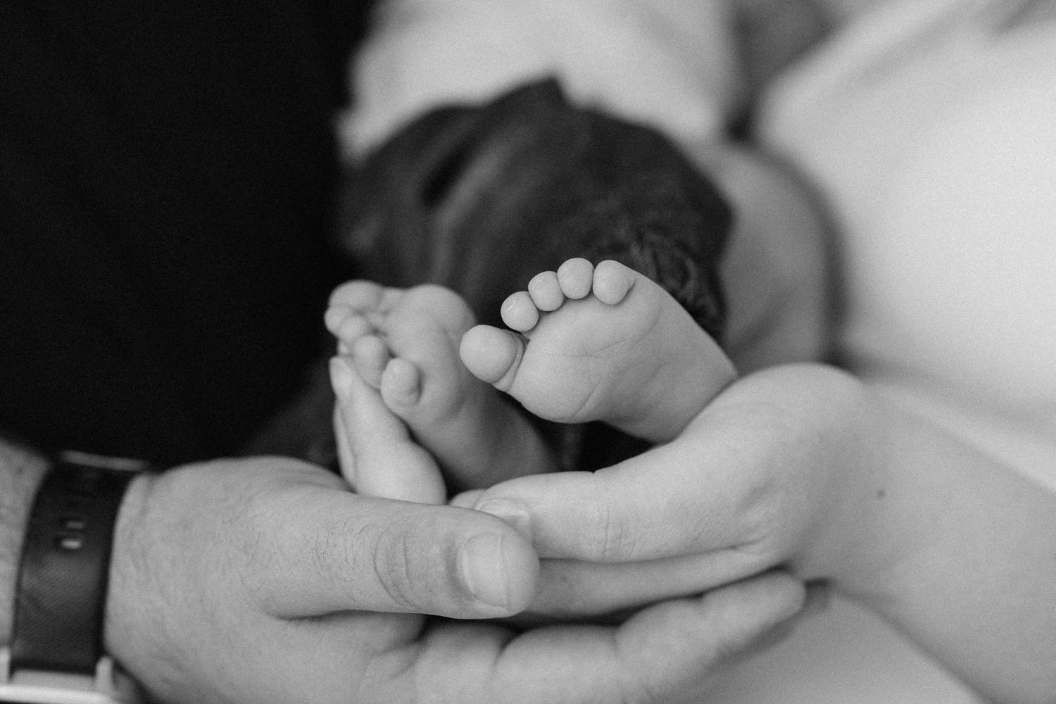 Black and white photo of newborn baby feet cradled gently in parents hands.