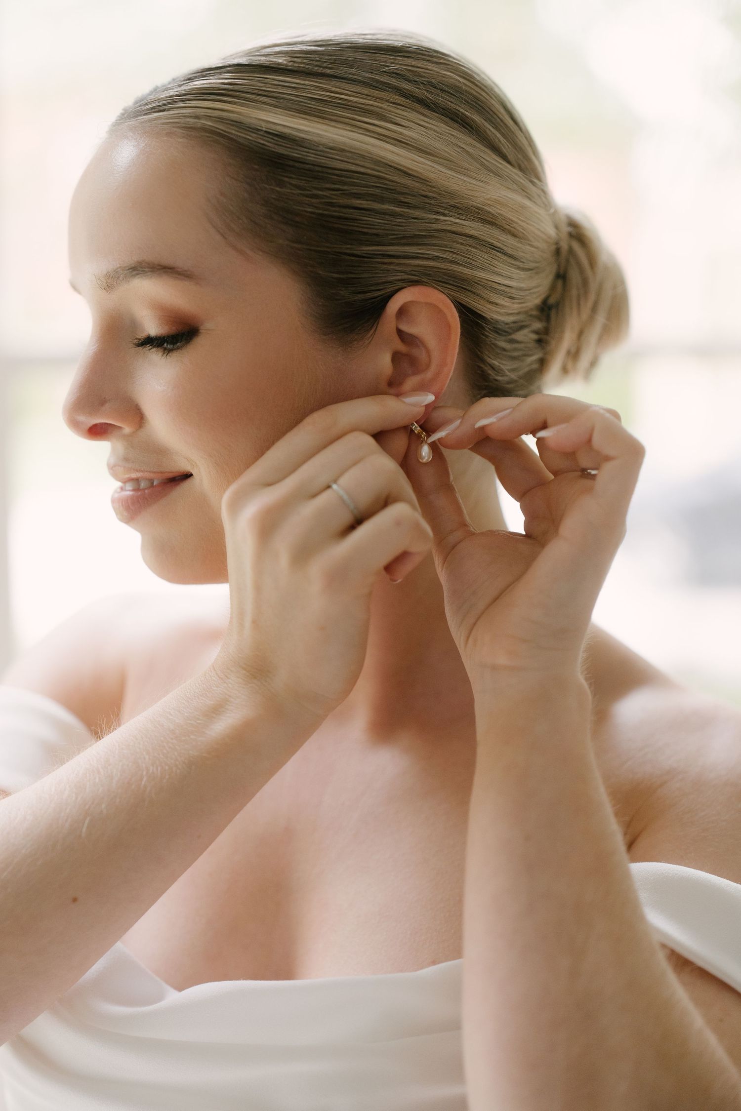 Bride smiling while putting on delicate drop earrings on her wedding morning in Guelph.