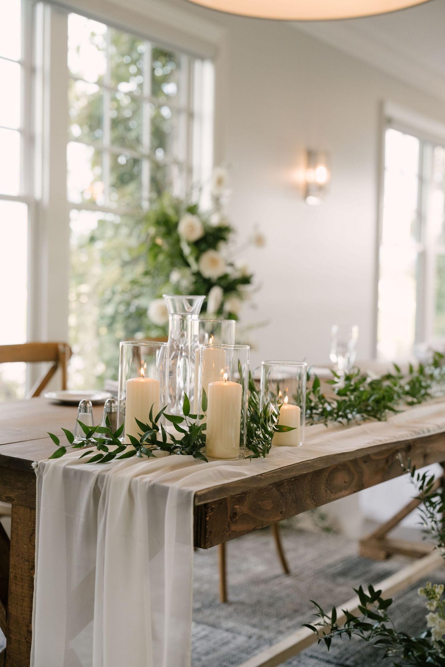 Rustic wood sweetheart table styled with white pillar candles, greenery garland, and flowing chiffon runner.