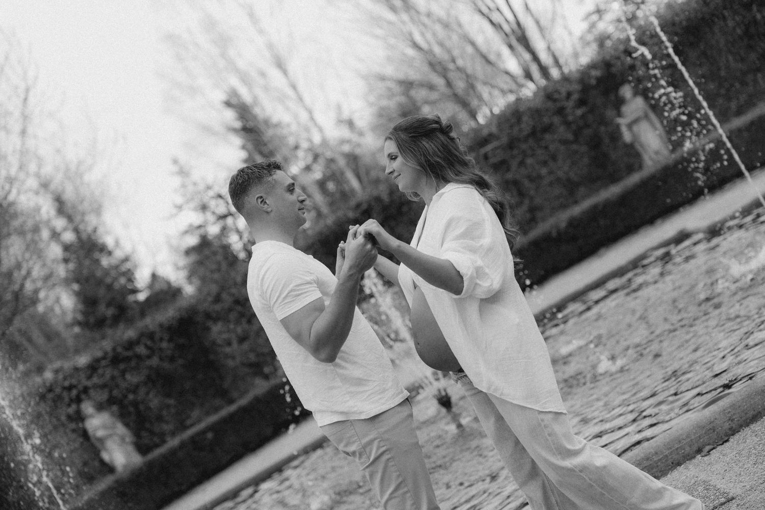 Black and white photo of a couple holding hands and dancing near a fountain in a garden.