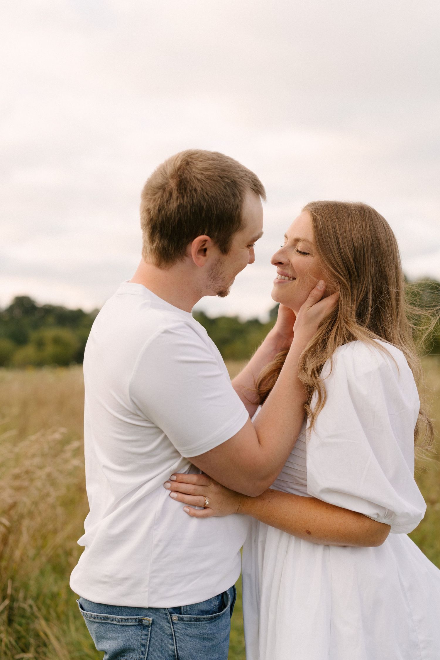 Couple in white outfits sharing a tender moment in a golden field, man gently holding woman's face.