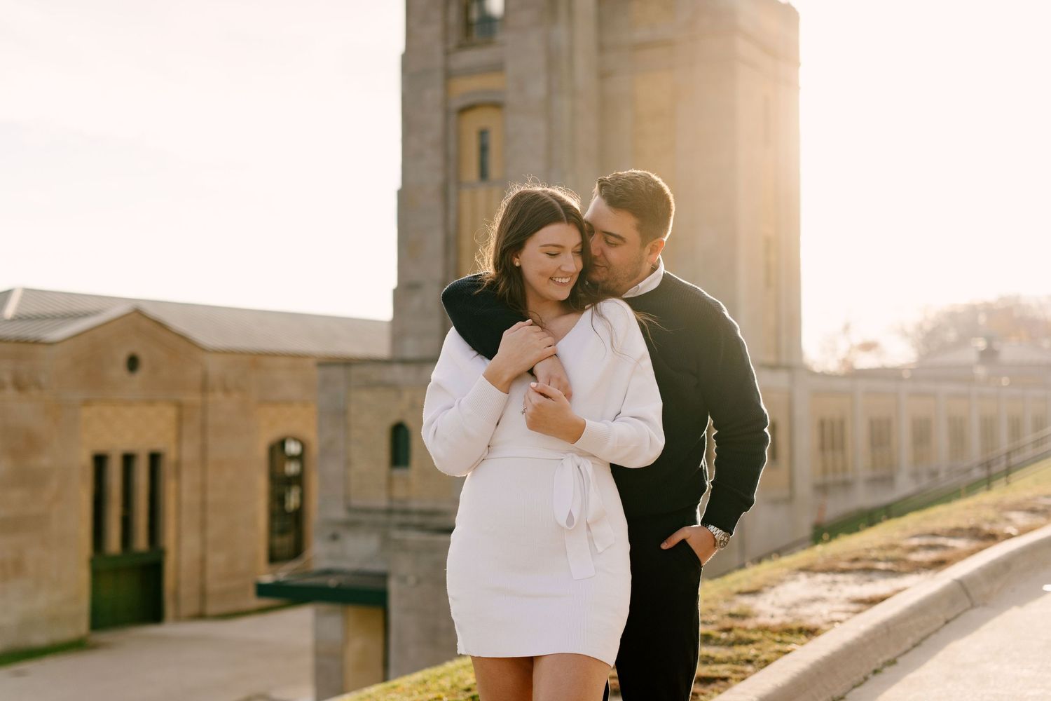 Couple embracing tenderly at golden hour with historic stone building in background.