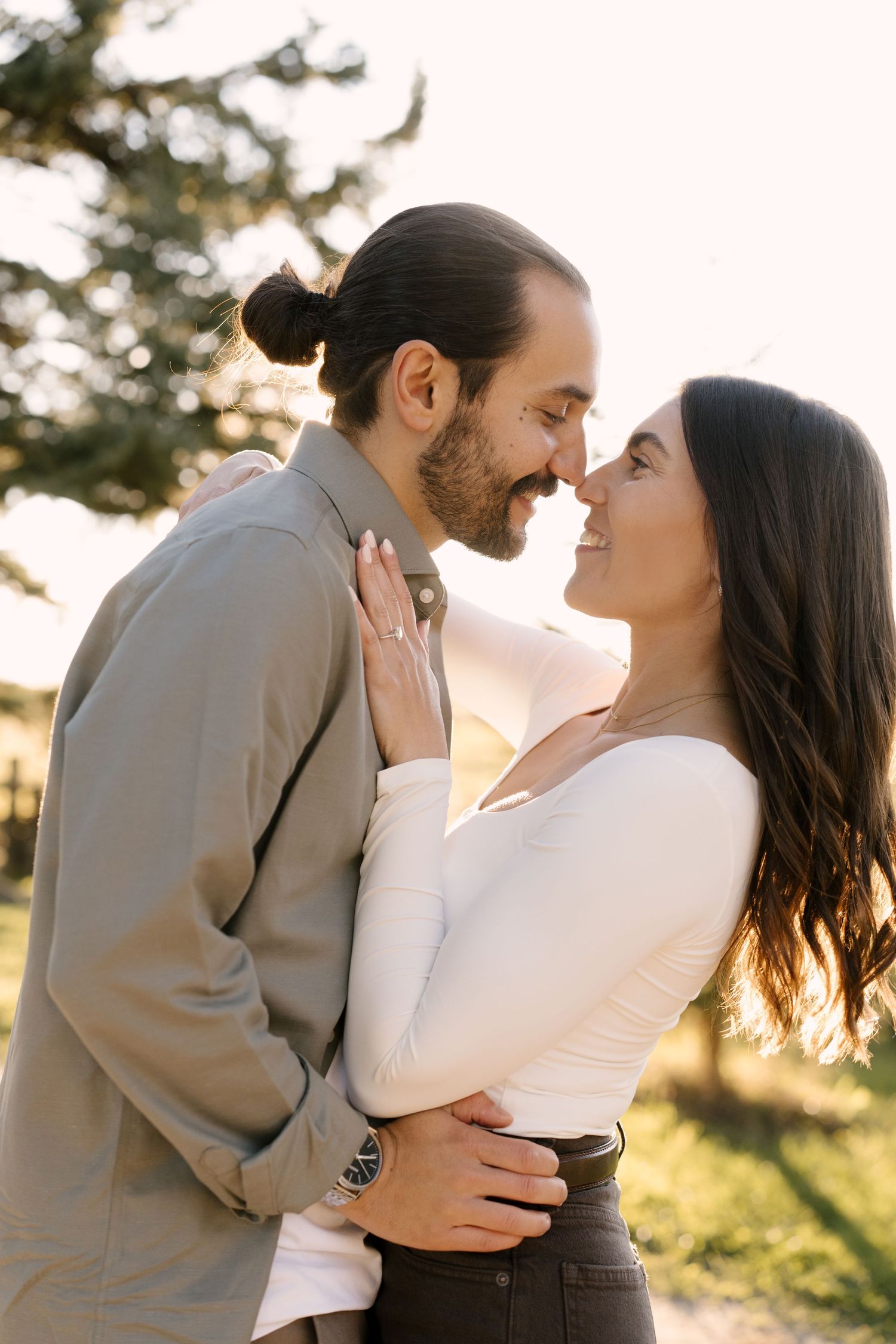 Happy couple touching noses and embracing in warm golden sunlight outdoors in a park.