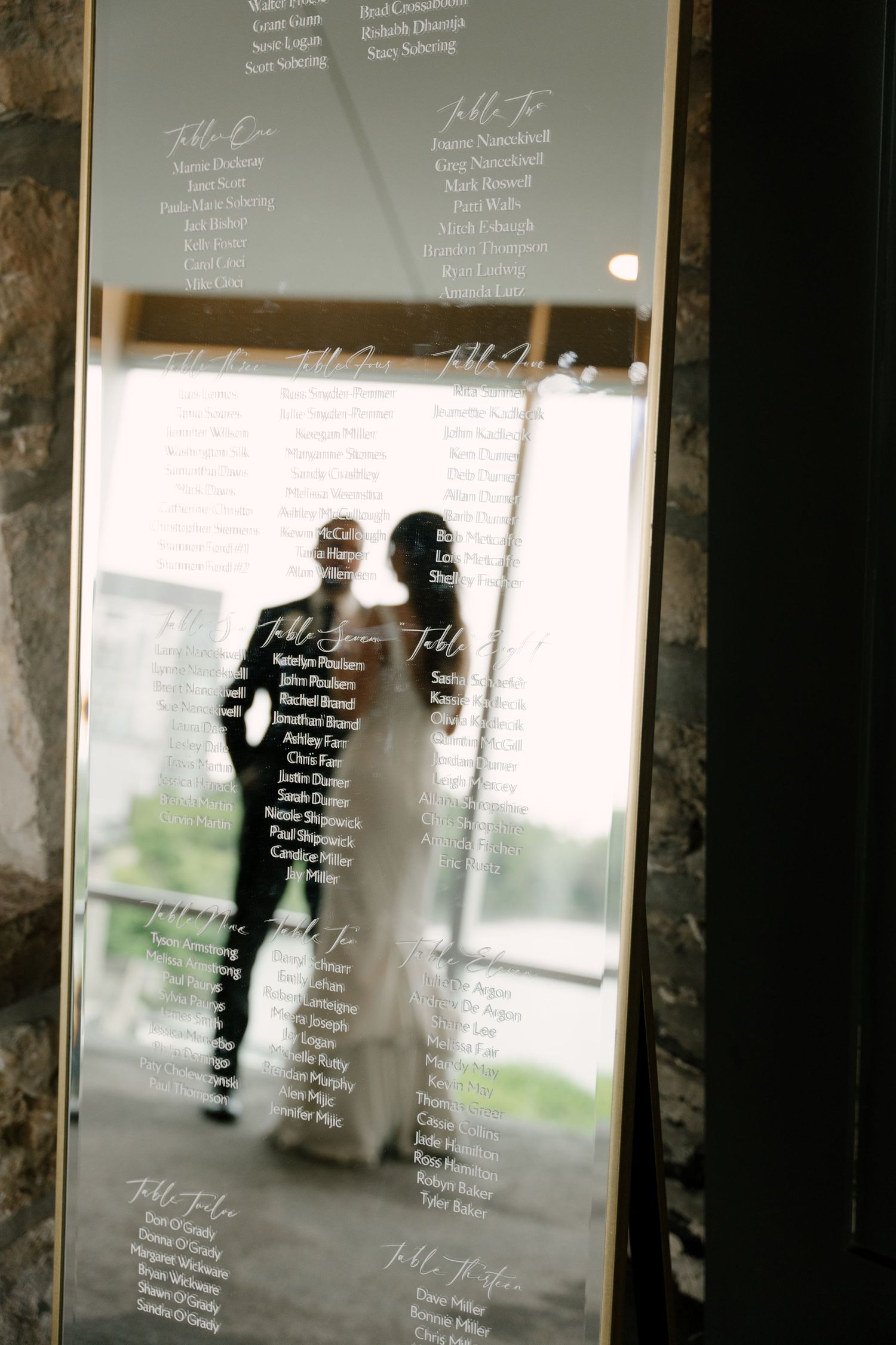 Wedding seating chart displayed on mirror reflecting bride and groom silhouette in elegant Cambridge Mill wedding venue.