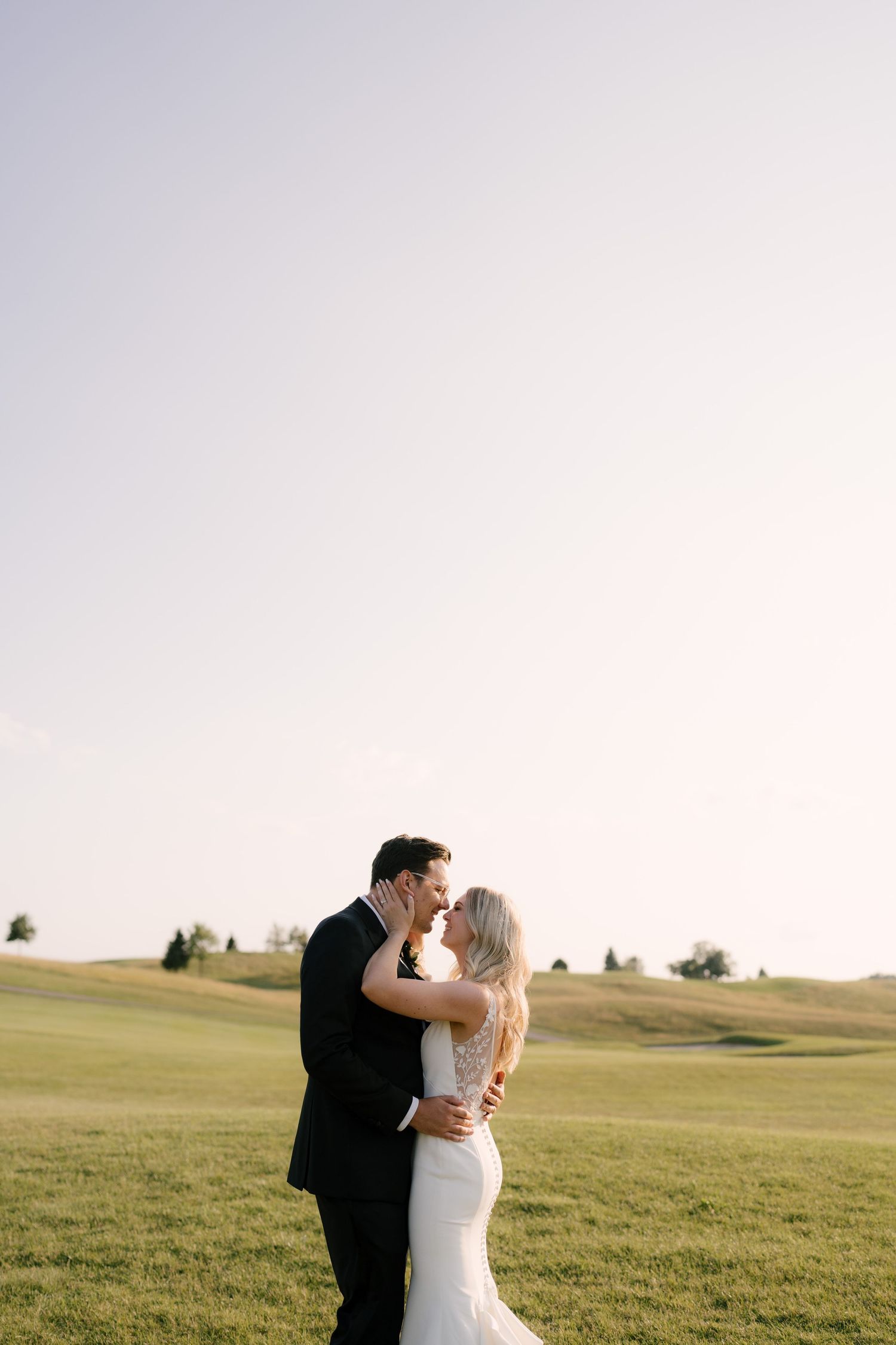 Bride and groom embracing and about to kiss on a wide open green Whistle Bear golf course.