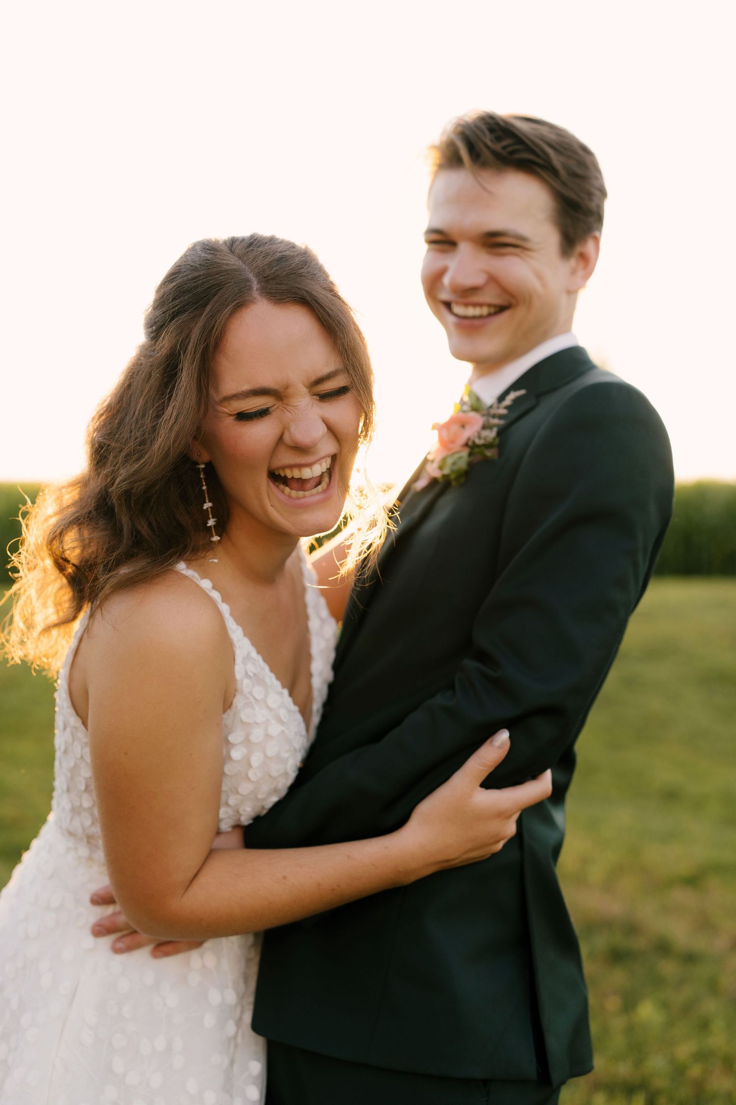 Joyful bride and groom laughing together outdoors during golden hour sunset portrait session.