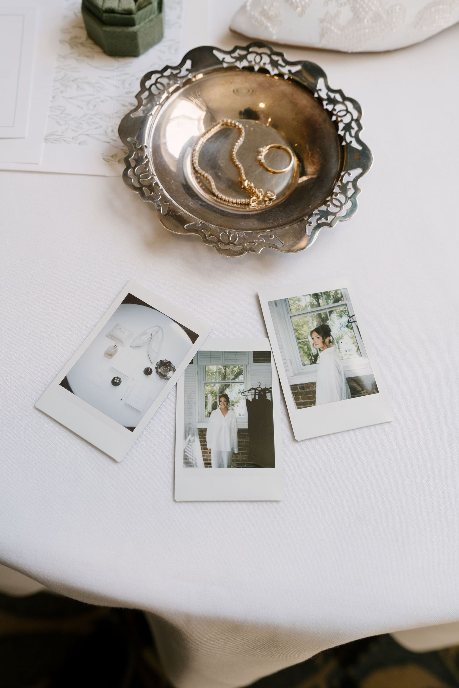 Polaroid photos and a silver tray with pearl jewelry and rings on a white tablecloth at a wedding.