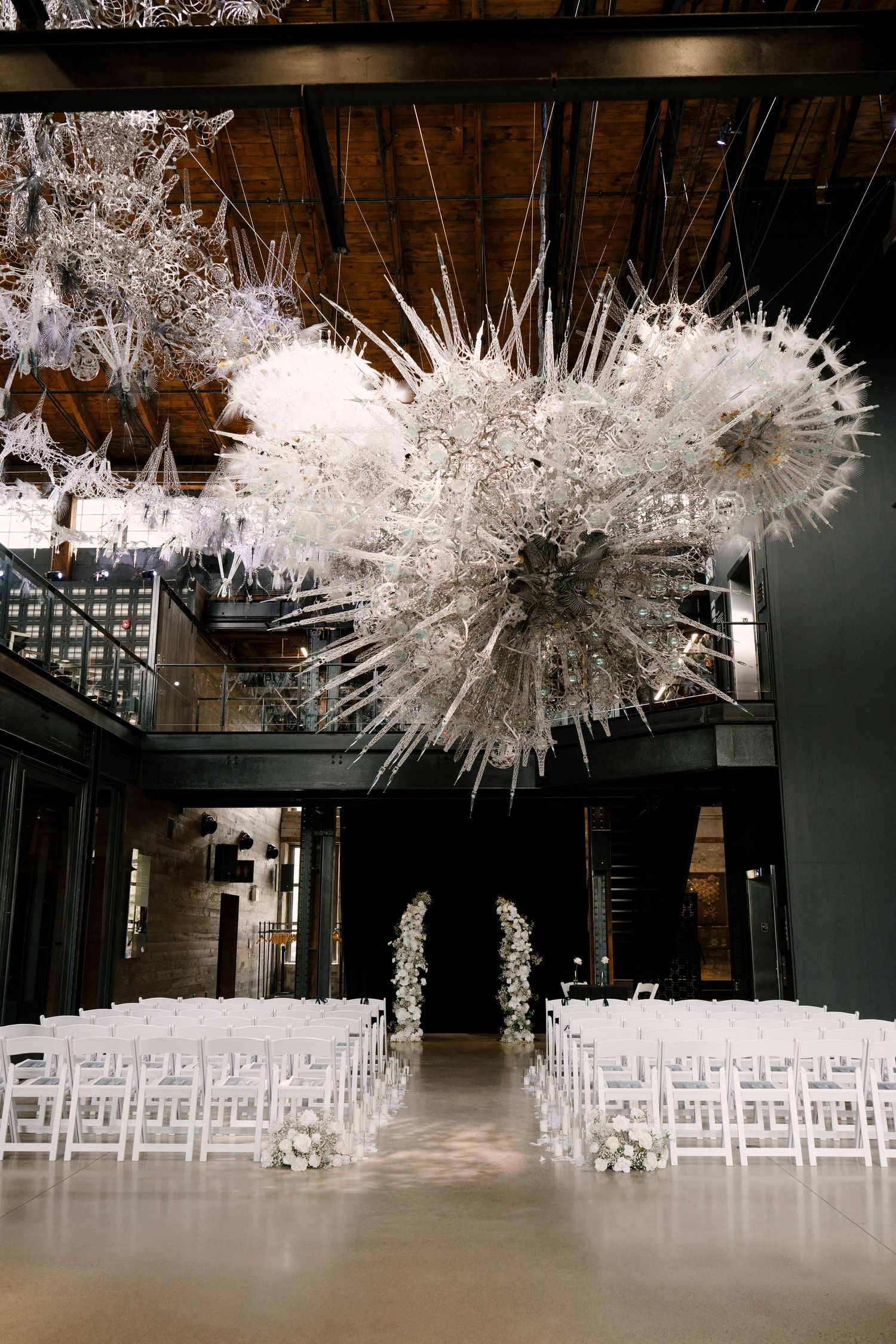 Elegant indoor wedding ceremony setup with white chairs, floral arch, and dramatic white sculptural ceiling installations at Tapestry Hall.