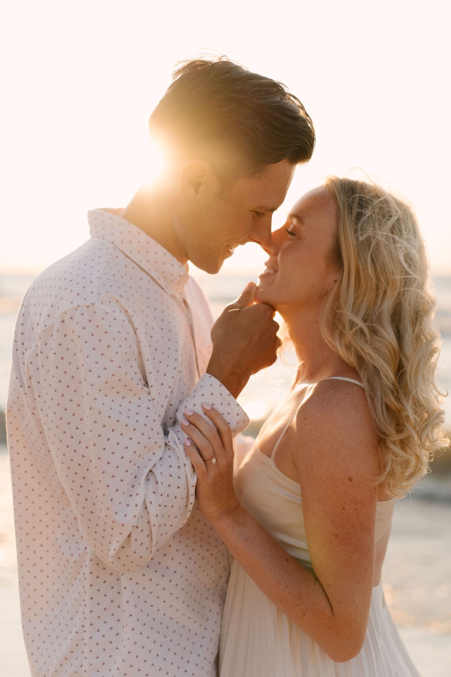 Couple sharing an intimate moment nose-to-nose with golden sunset backlight on the beach.