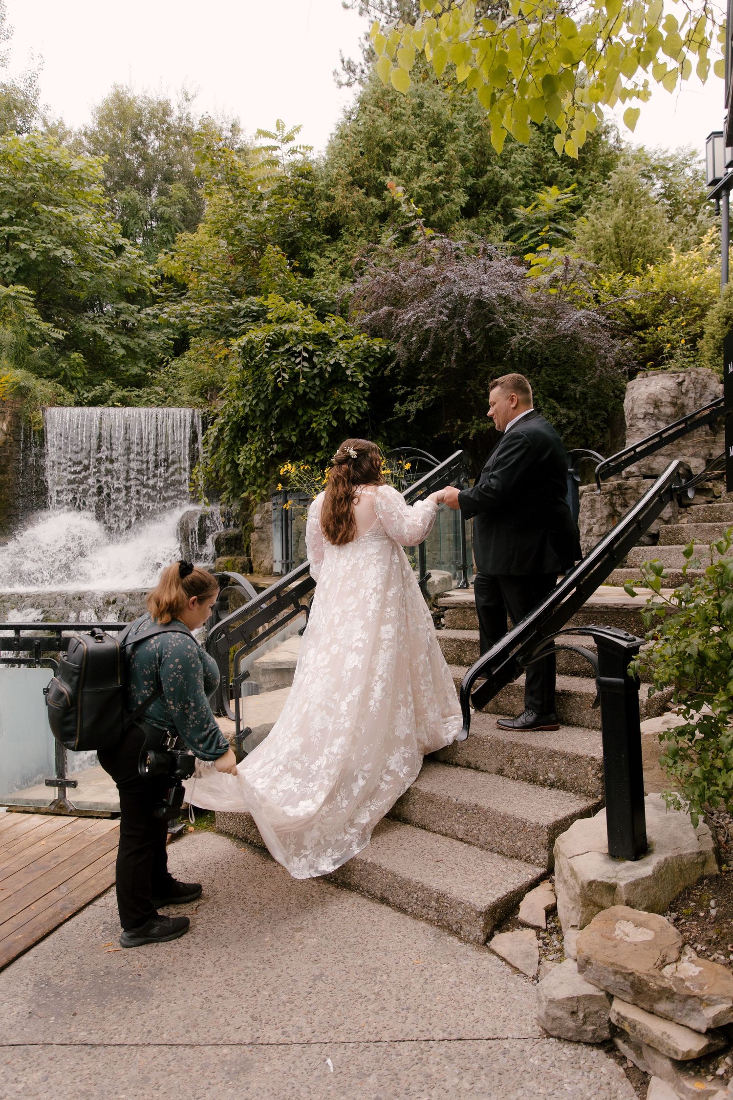 Photographer captures bride and groom exchanging vows on stone steps near a waterfall.
