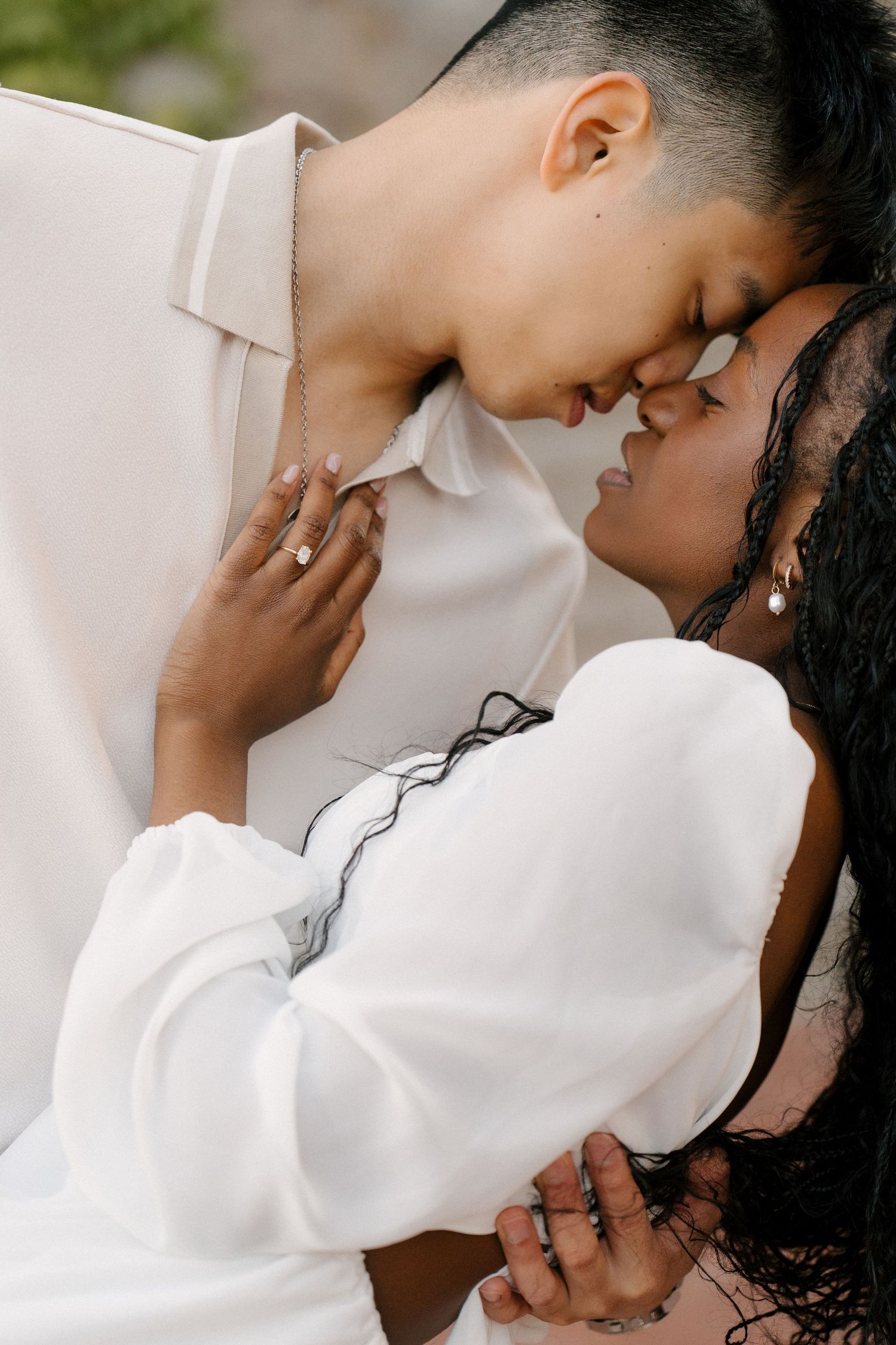 Interracial couple in white outfits sharing an intimate forehead-to-forehead moment.