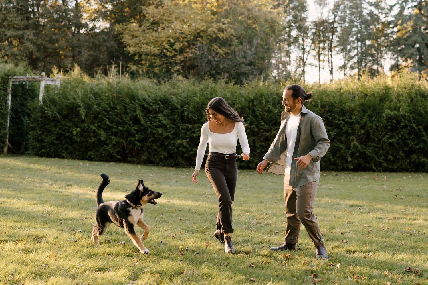 Couple playing with their energetic German Shepherd dog on a green lawn in a park.