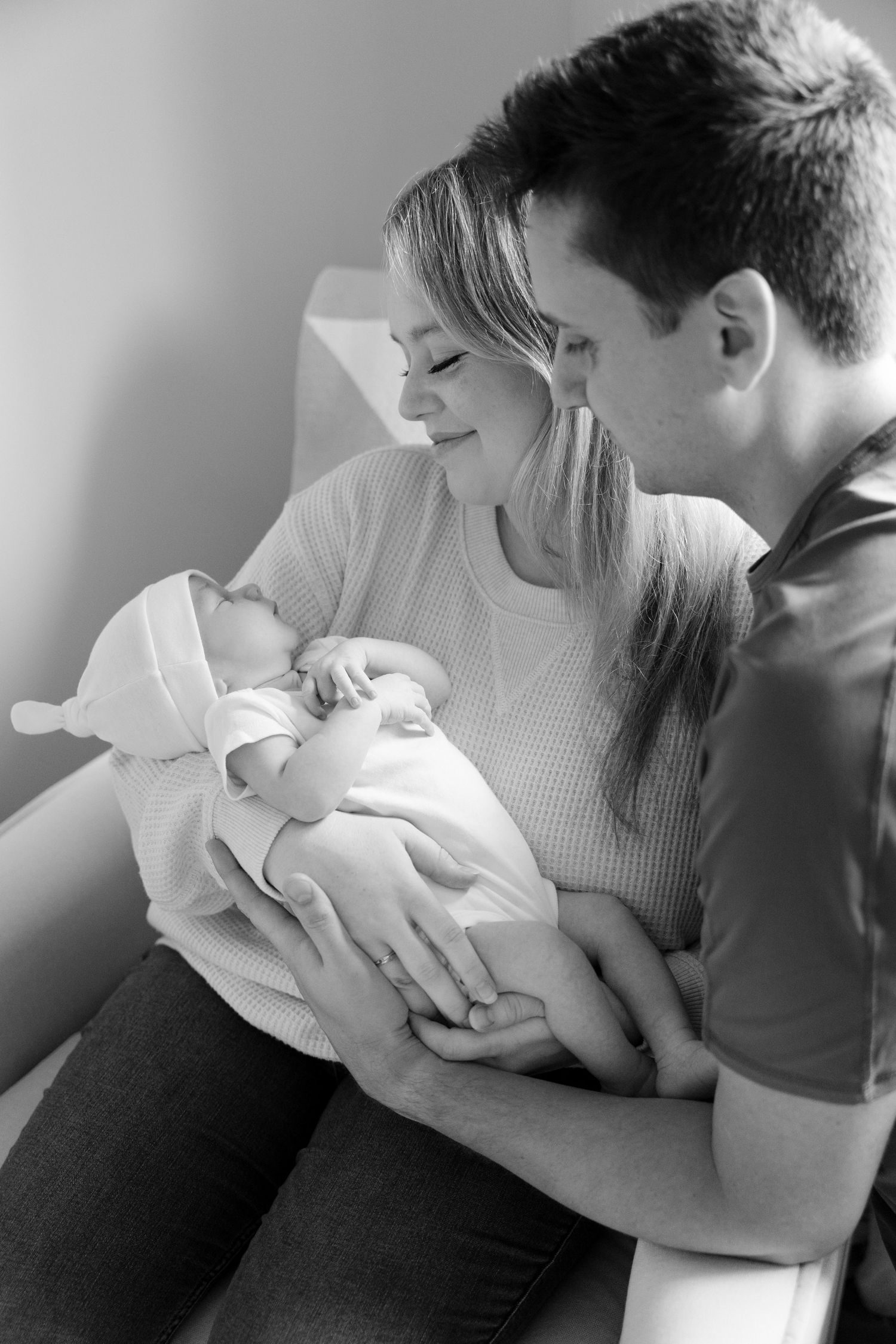 Black and white portrait of new parents sitting together tenderly holding their sleeping newborn baby.