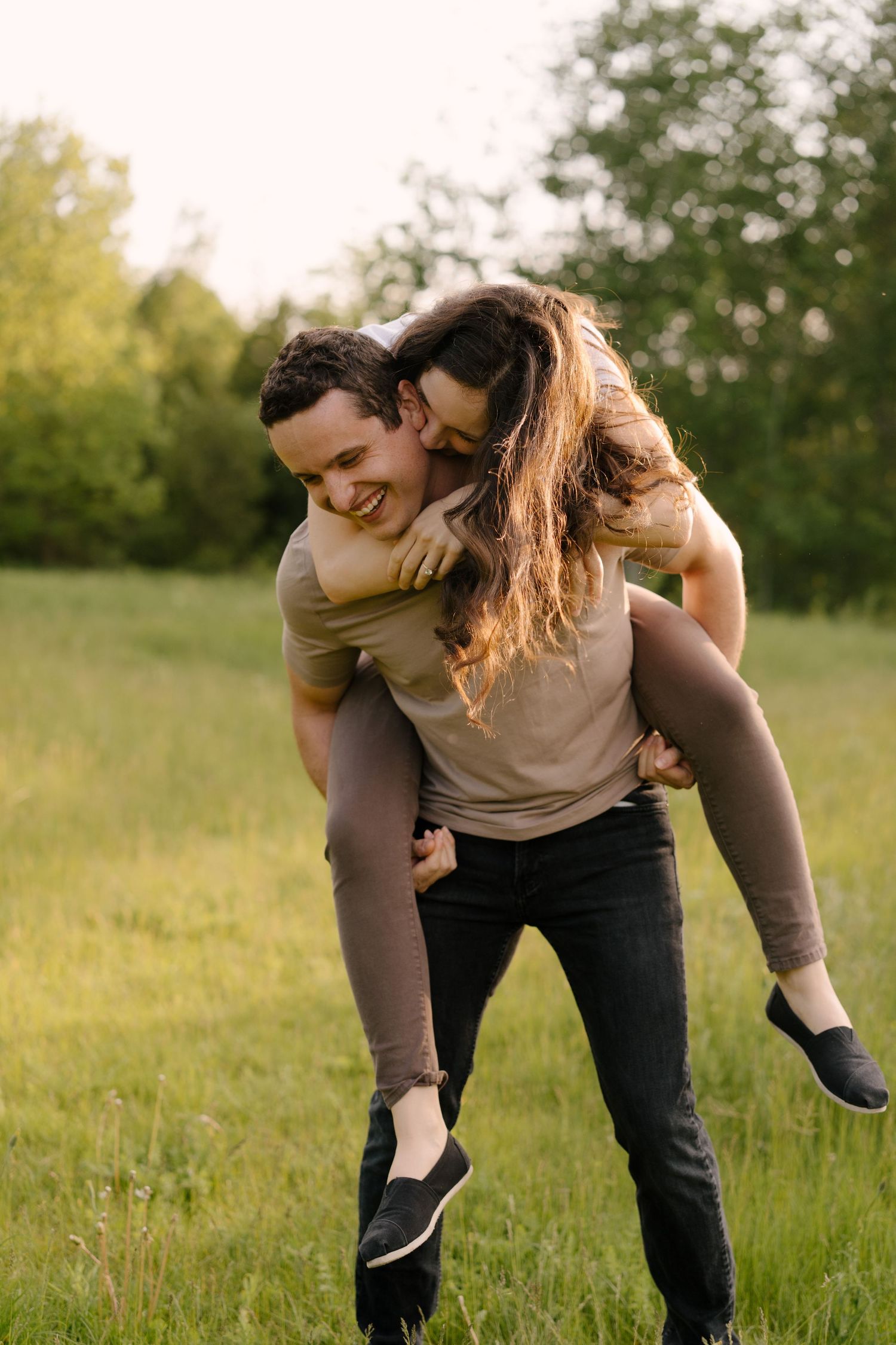 Joyful couple in a sunny green field, man giving laughing woman a piggyback ride outdoors.