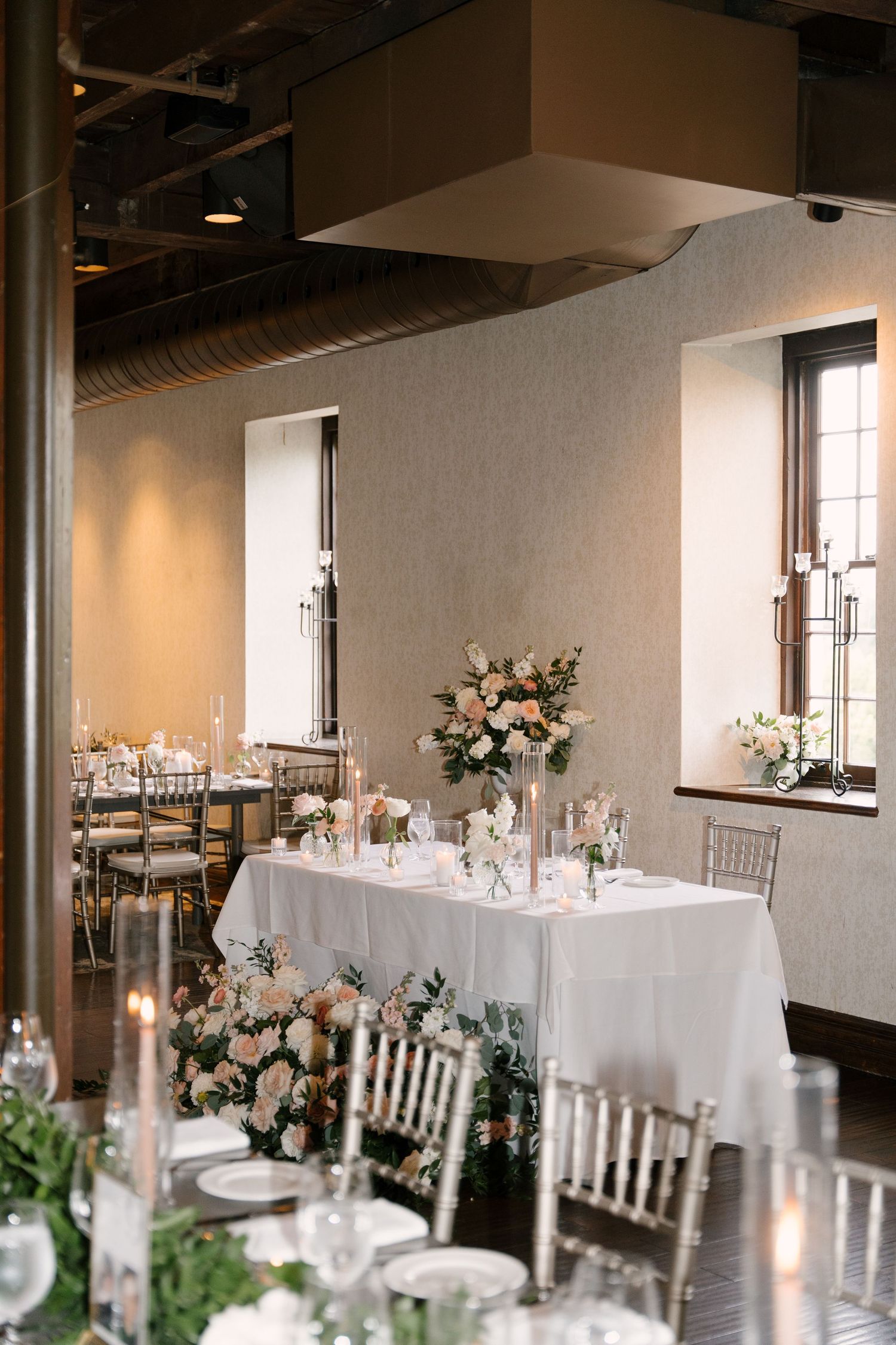 Elegant Ancaster Mill wedding reception head table adorned with tall floral arrangements of blush roses and candles.