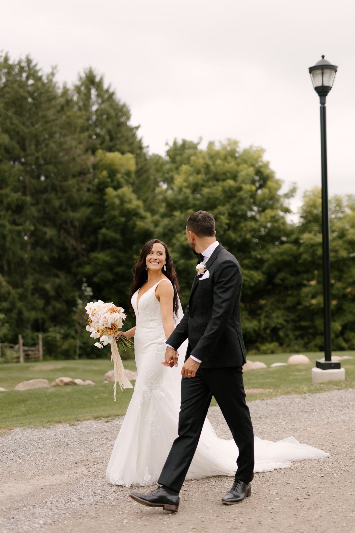 Smiling bride and groom walking hand in hand along a gravel path at Wakefield Estates gardens.