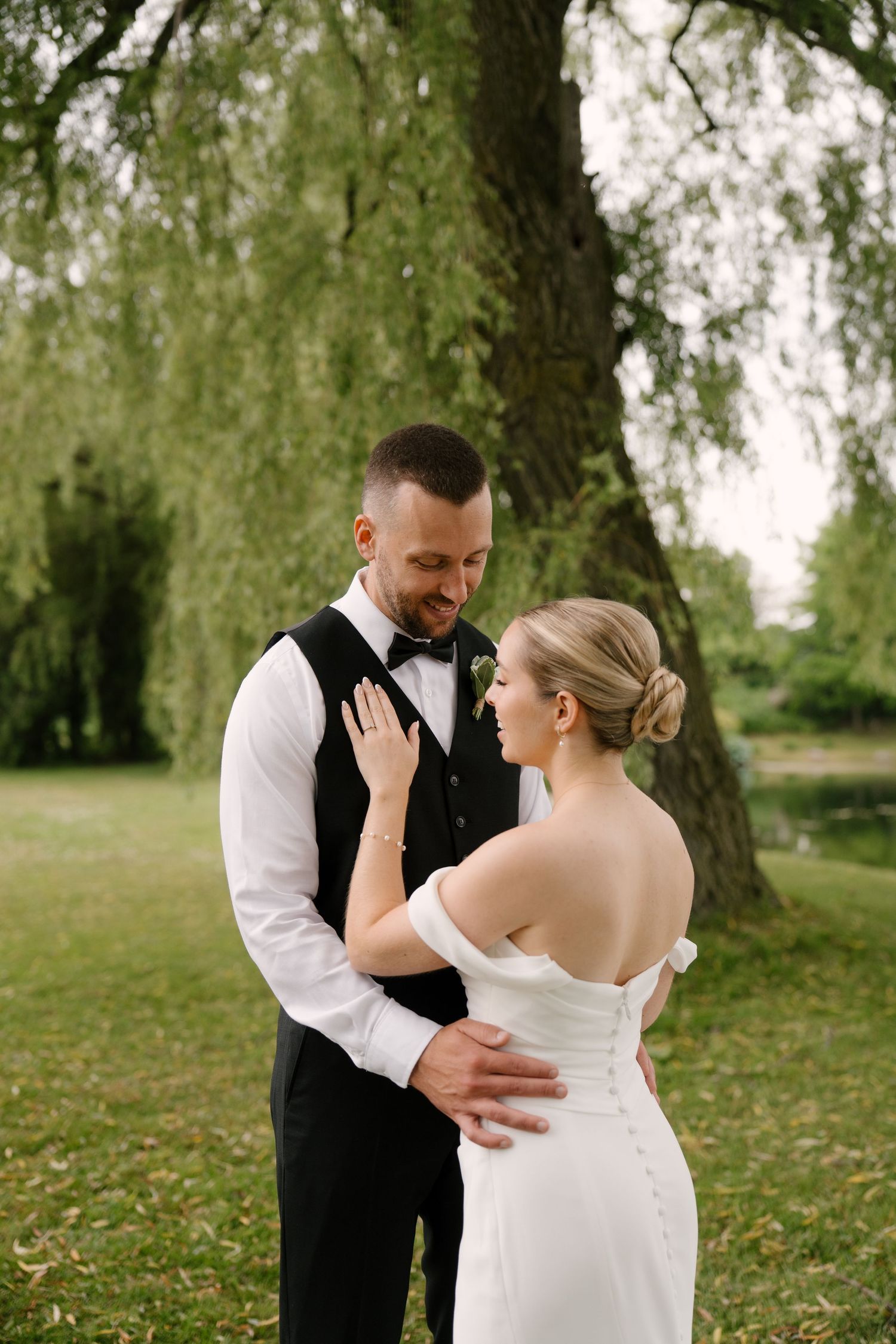 Bride and groom share a tender embrace under a weeping willow tree during their outdoor wedding portrait session in Guelph.