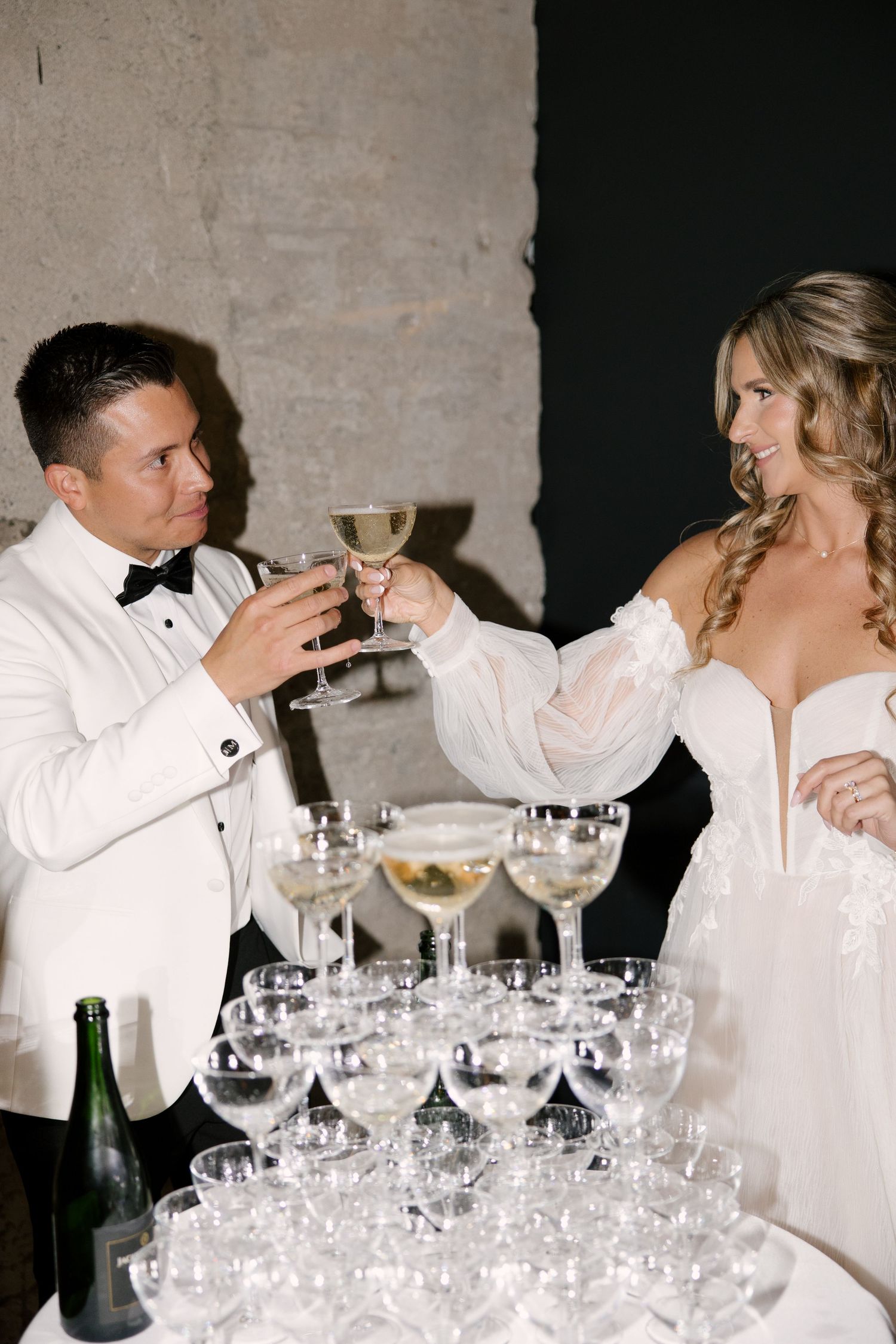 Bride and groom toasting with champagne glasses beside a sparkling champagne tower at Tapestry Hall venue.