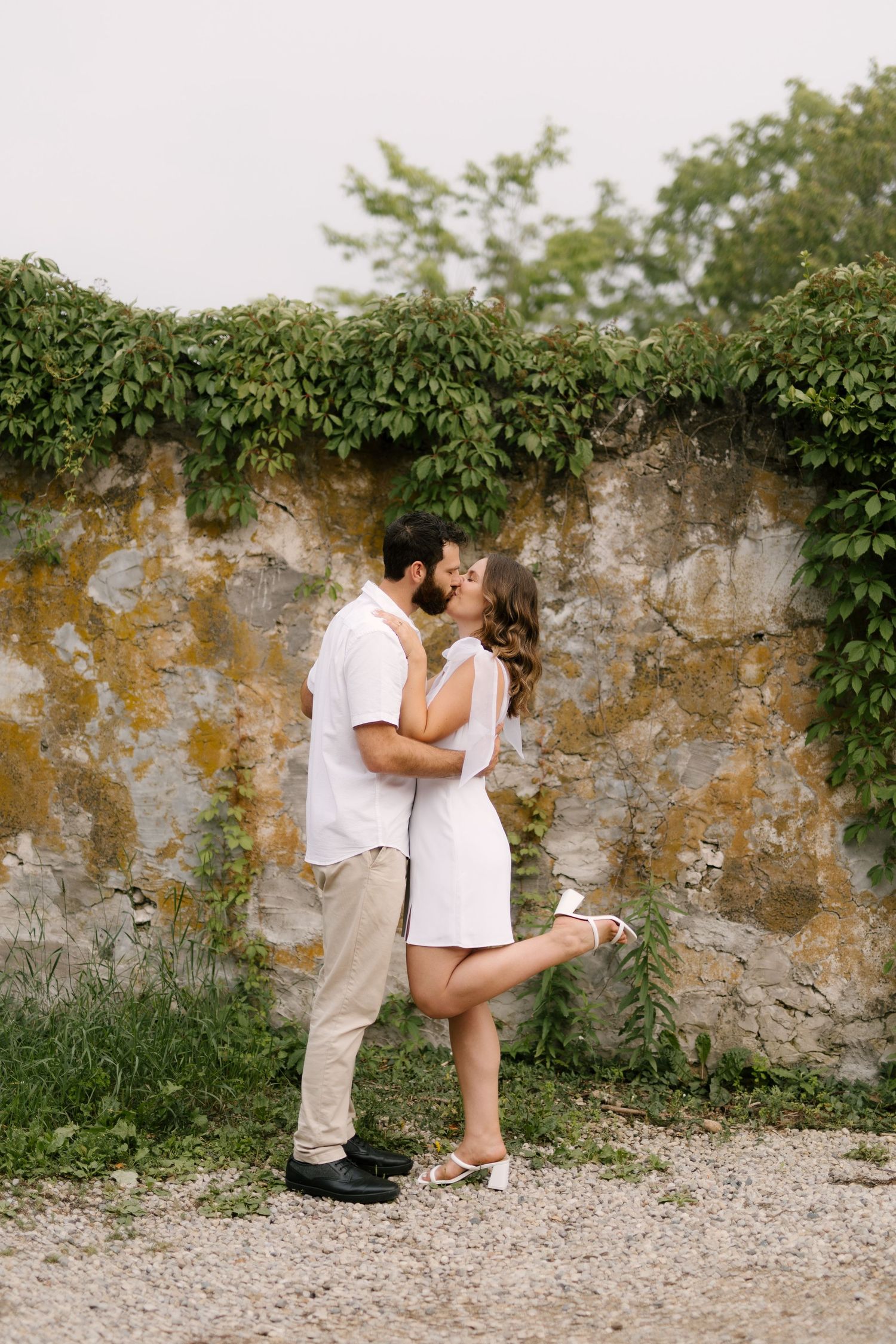 Romantic couple sharing a kiss against an ivy-covered stone wall outdoors.