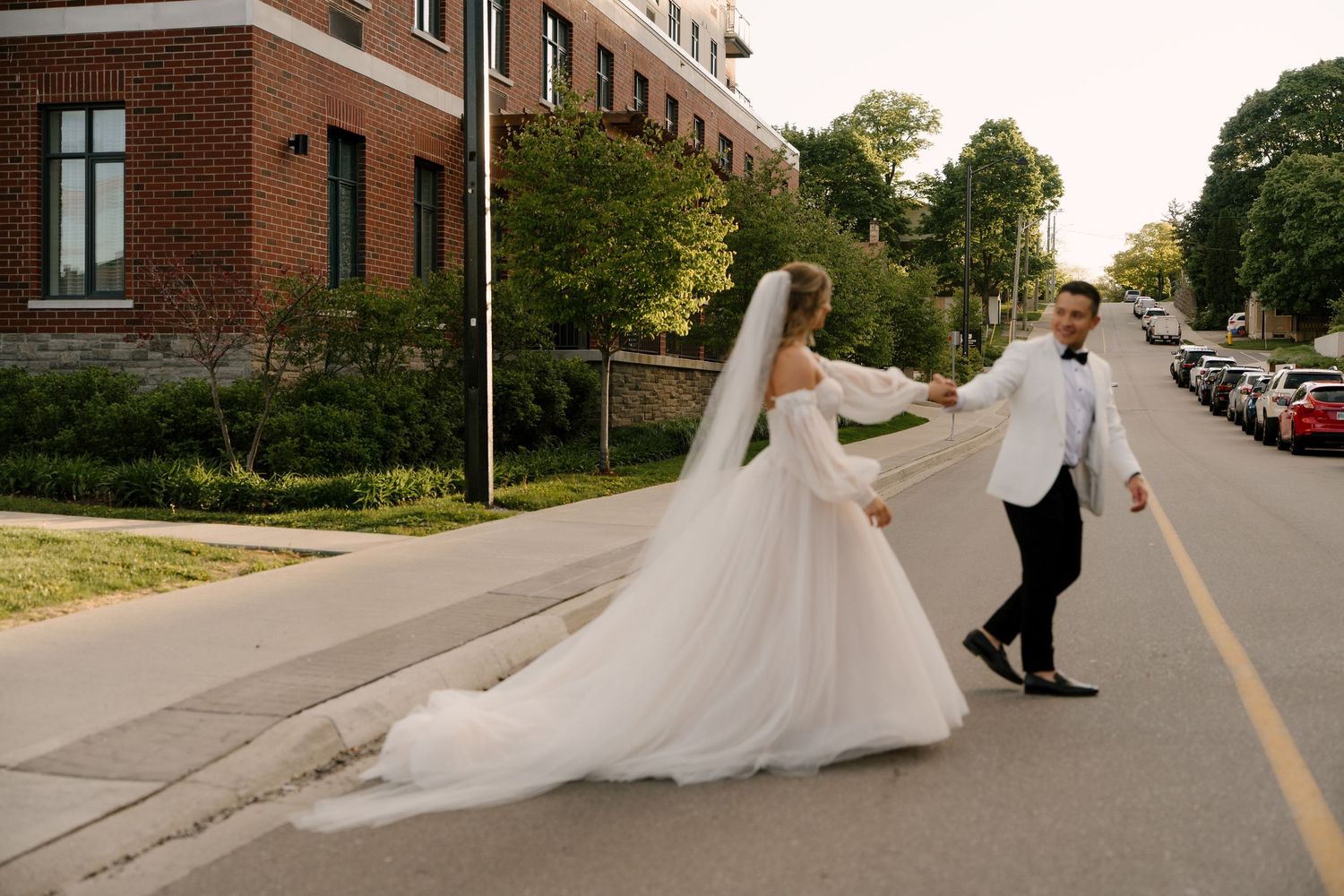 Bride in flowing white gown and groom in tuxedo walking hand in hand on street at Tapestry Hall wedding venue.