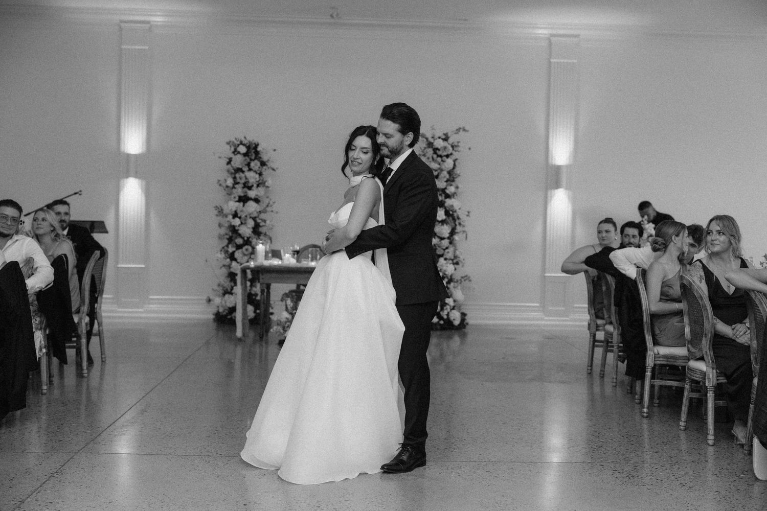 Black and white photo of newlyweds dancing together as guests watch at elegant Roseville Estates wedding reception.