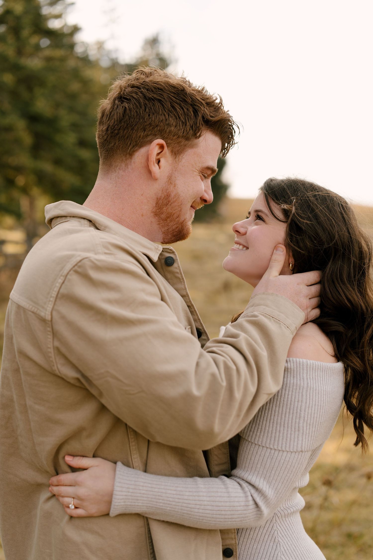 Couple sharing a romantic embrace outdoors, man gently tucking womans hair back while she smiles.