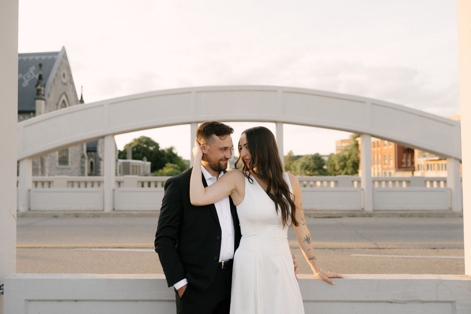 Bride and groom sharing a tender moment on a white arch bridge at sunset.