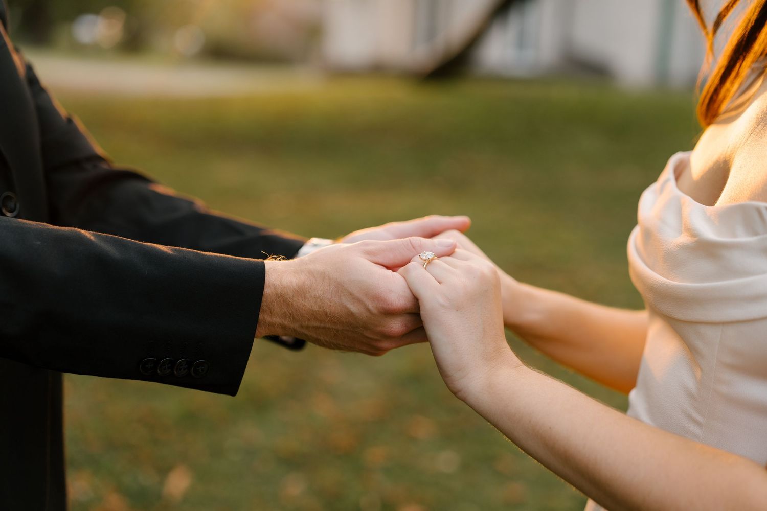 Close-up of a couple holding hands outdoors during a wedding ceremony, with a blurred green garden background.